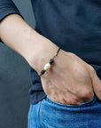 Close-up of a men’s pearl leather bracelet with lava stone accents worn on a model’s wrist