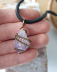 Men’s raw amethyst pendant on black leather cord shown in hand for size reference, antique bronze copper wire wrapped crystal necklace