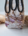Three raw amethyst pendants on black leather cords showing natural variation in size, shape and purple tone, antique bronze wire wrapped