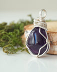 Side view detail of polished dark amethyst pendant with sterling silver wire wrapping, handmade necklace