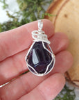 Natural dark amethyst pendant held in hand for size reference, handmade silver plated wire wrapped necklace