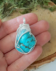 Raw turquoise pendant size in hand showing silver wire wrap detail