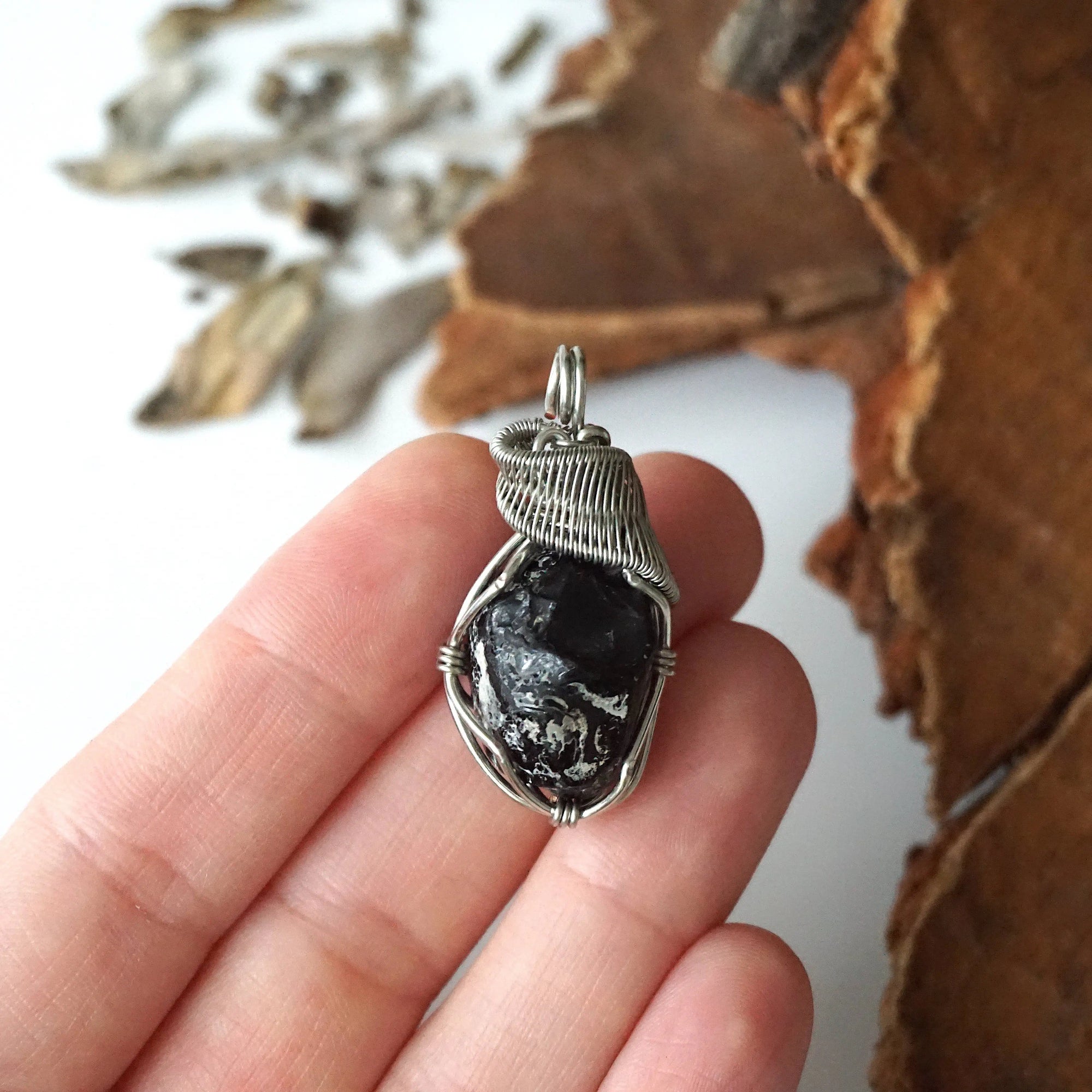 Apache tears obsidian pendant in hand for size reference – natural black volcanic glass, white gold copper wire, unisex jewelry by Designs by Nature Gems.