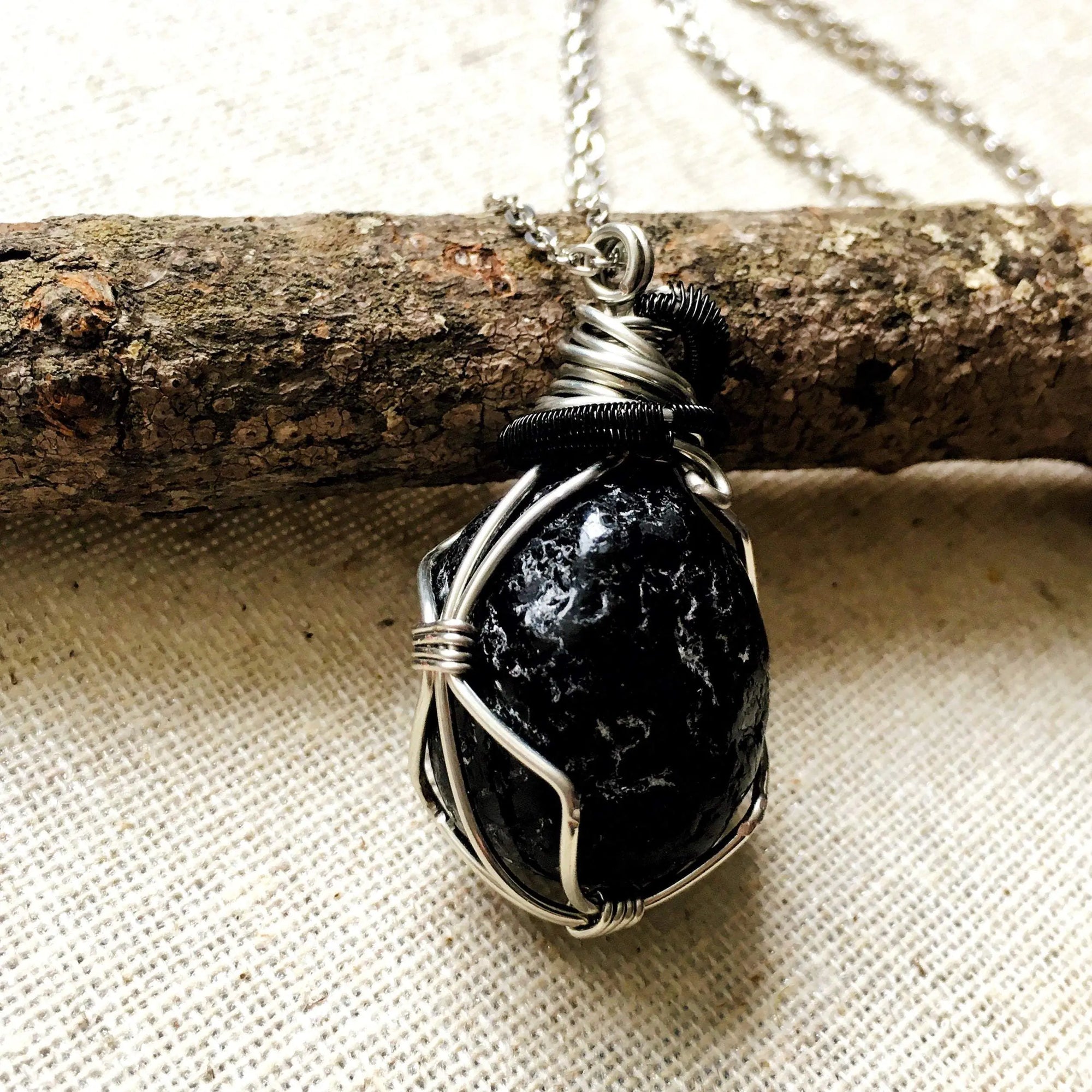 Angle view of apache tears obsidian necklace for men – highlighting unique artisan wire wrapping, glossy volcanic glass, white gold and black copper.