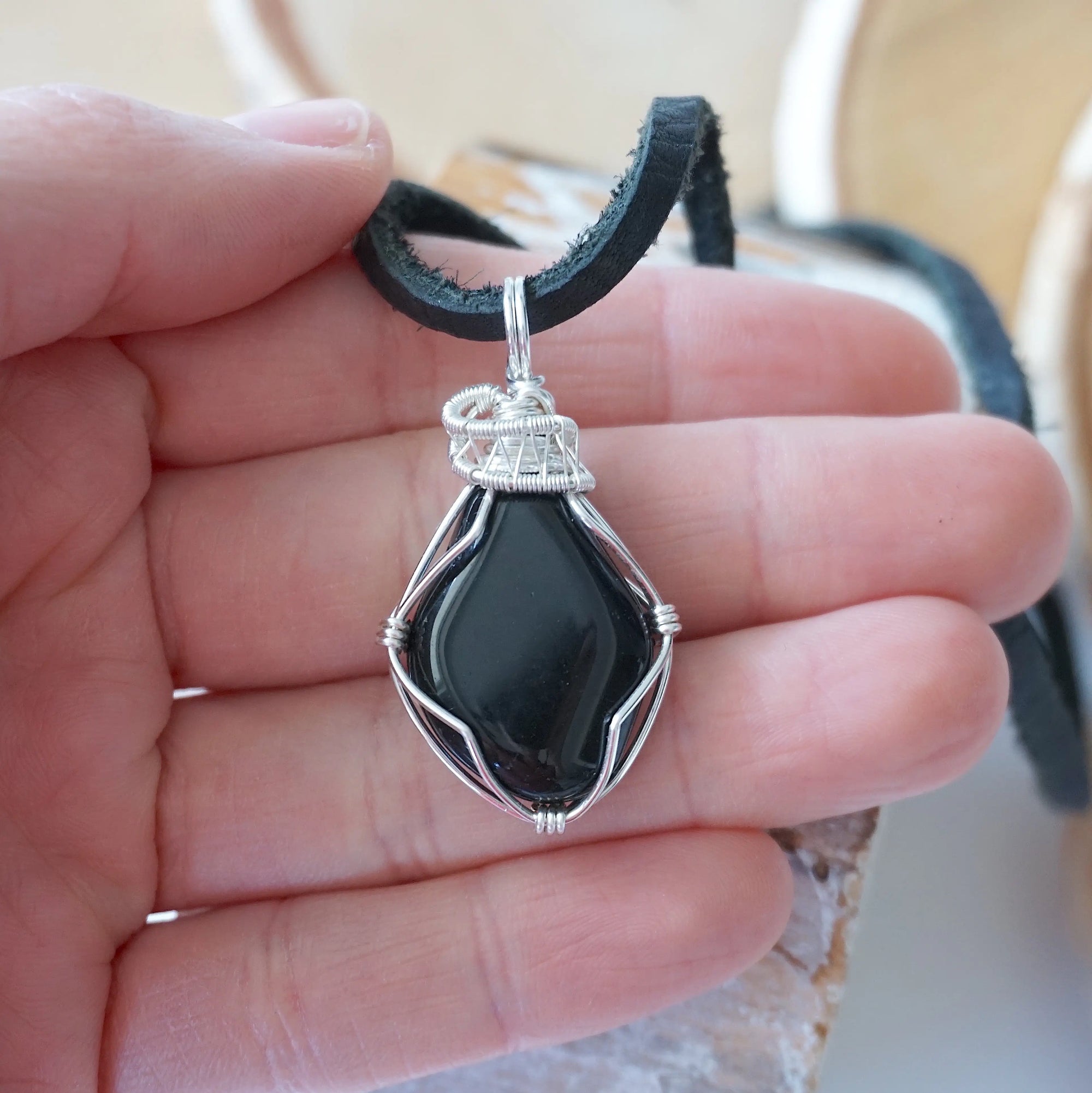 Black onyx necklace for men in hand for size reference – natural black crystal, silver copper wire, flat black leather cord, July birthstone.