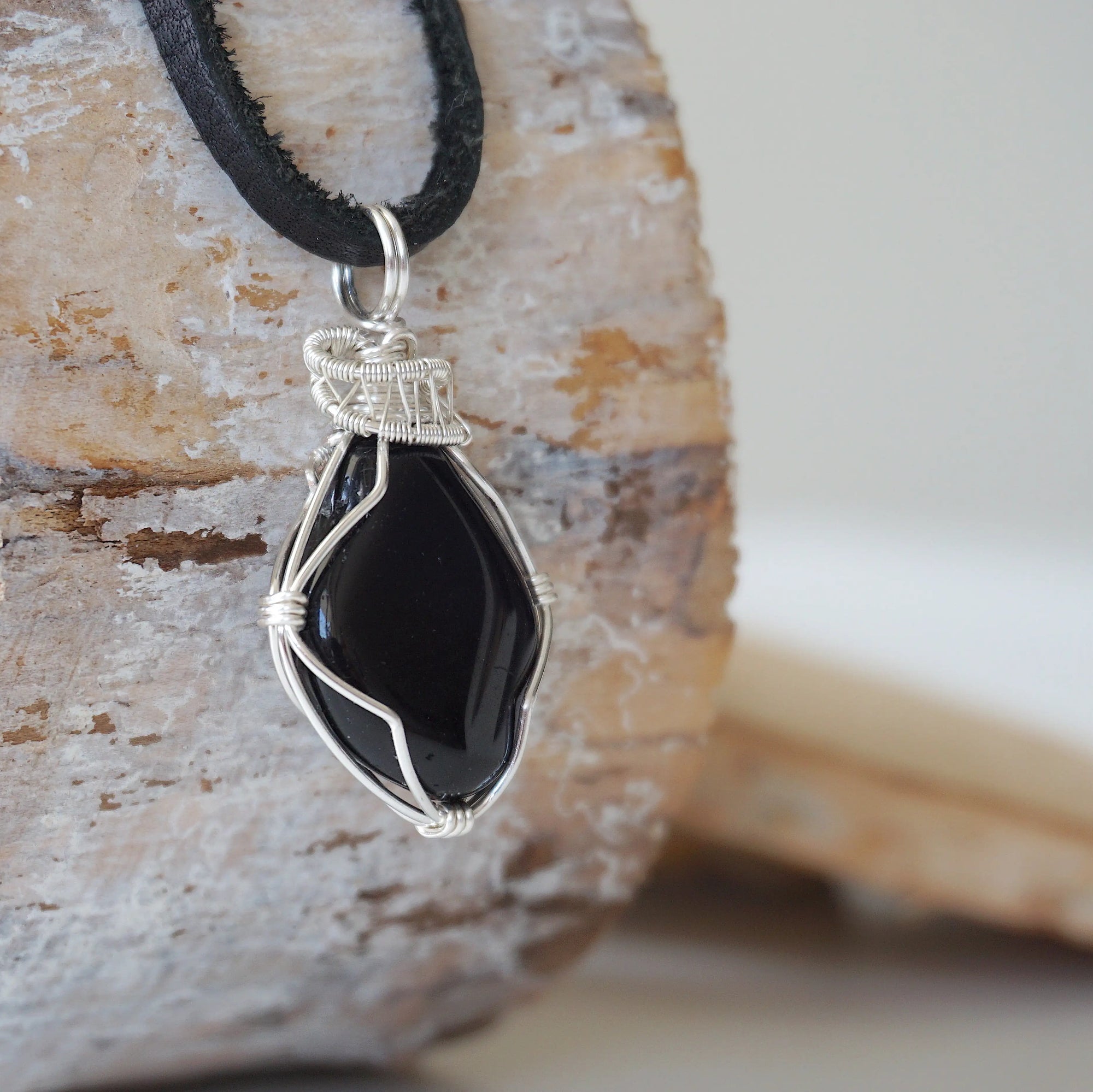 Right angle close-up of men's black onyx necklace – detailed silver copper wire wrapping, raw onyx, flat black leather cord.