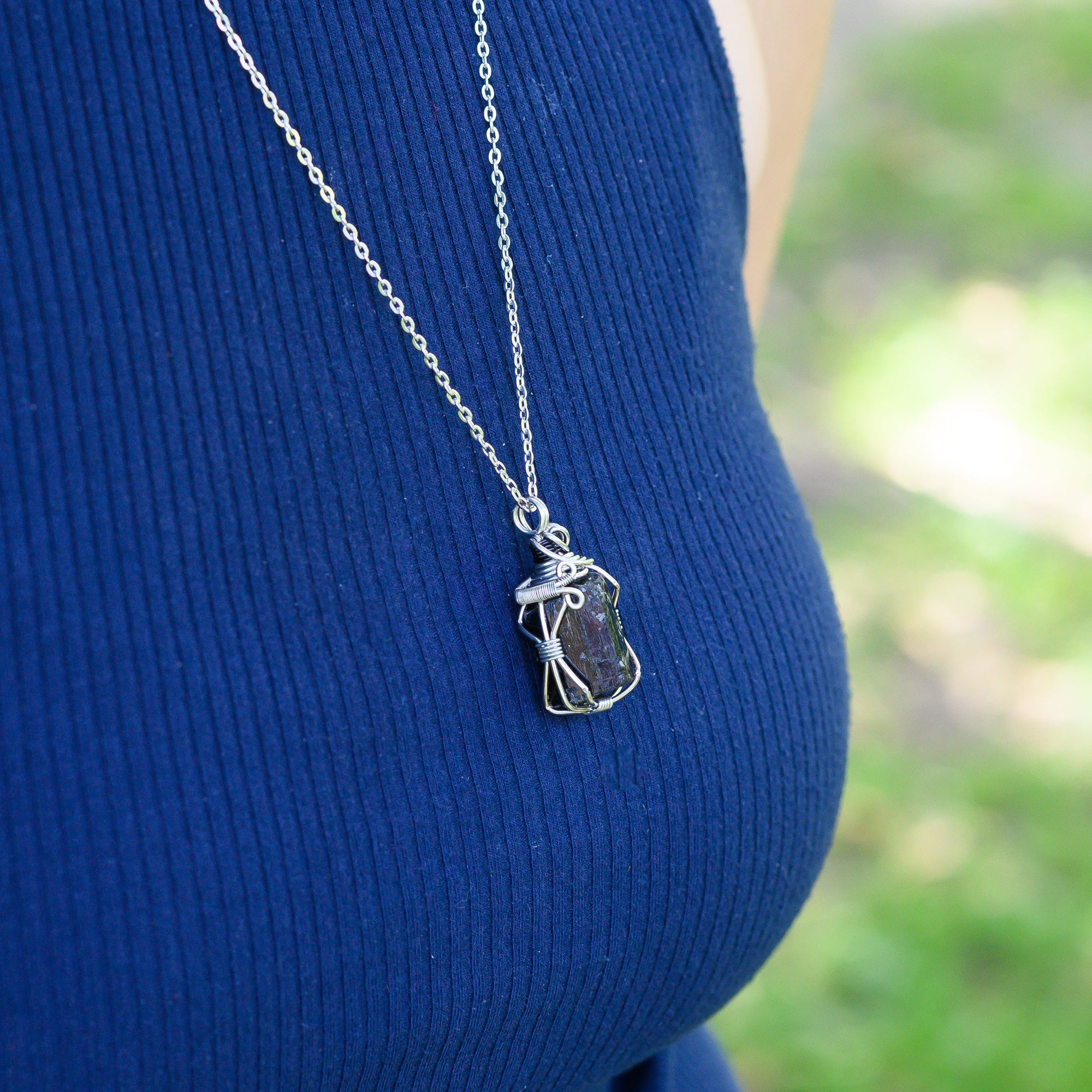 Person wearing a blue sleeveless top with a silver necklace featuring a pendant.