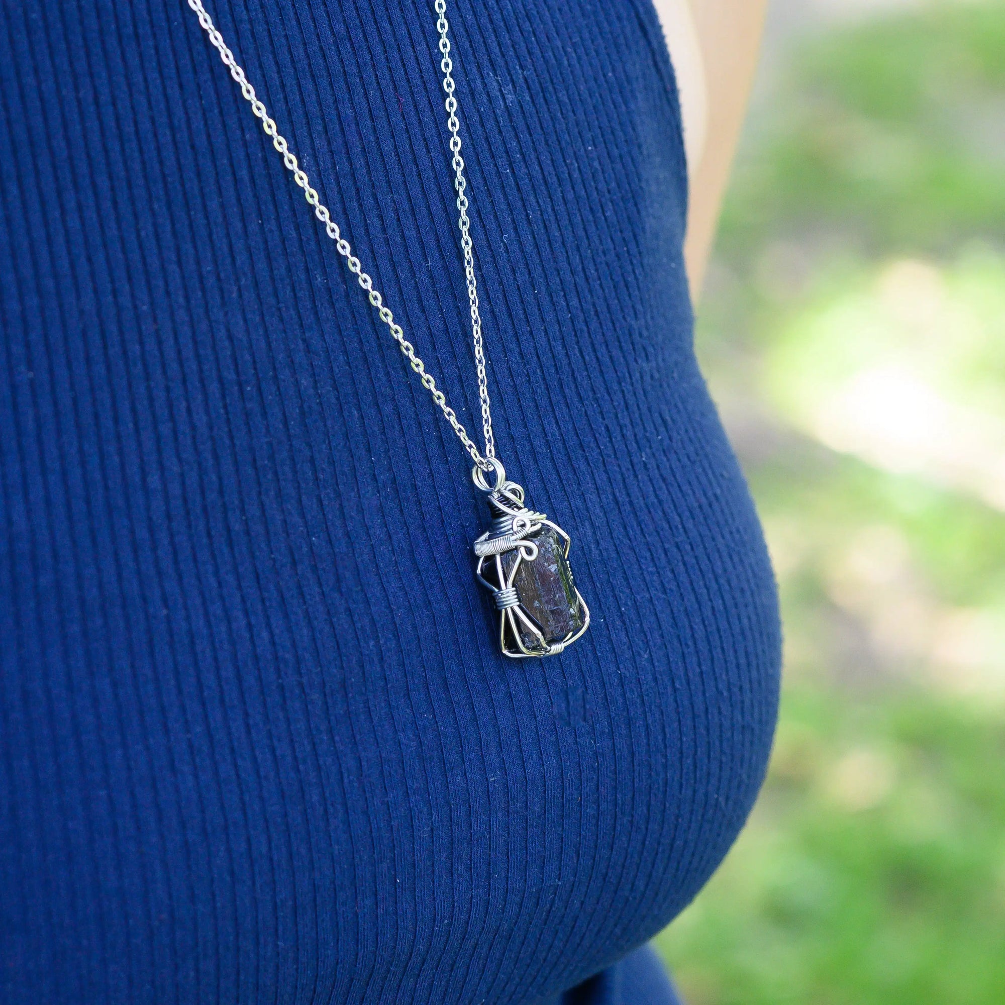 Person wearing a blue sleeveless top with a silver necklace featuring a pendant.