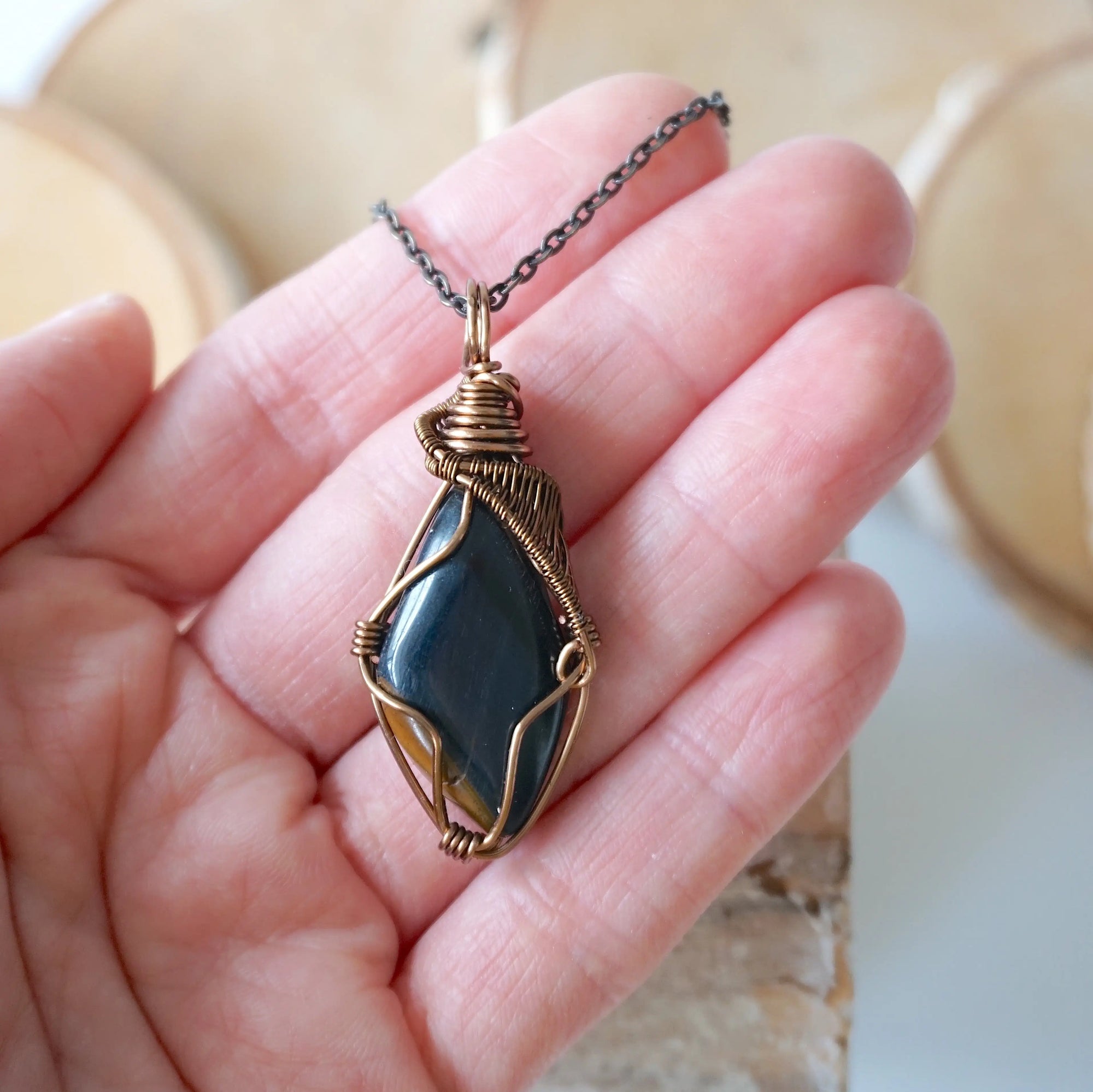 Blue tiger's eye necklace for men in hand for size reference – natural polished stone, antique bronze copper wire, masculine design.