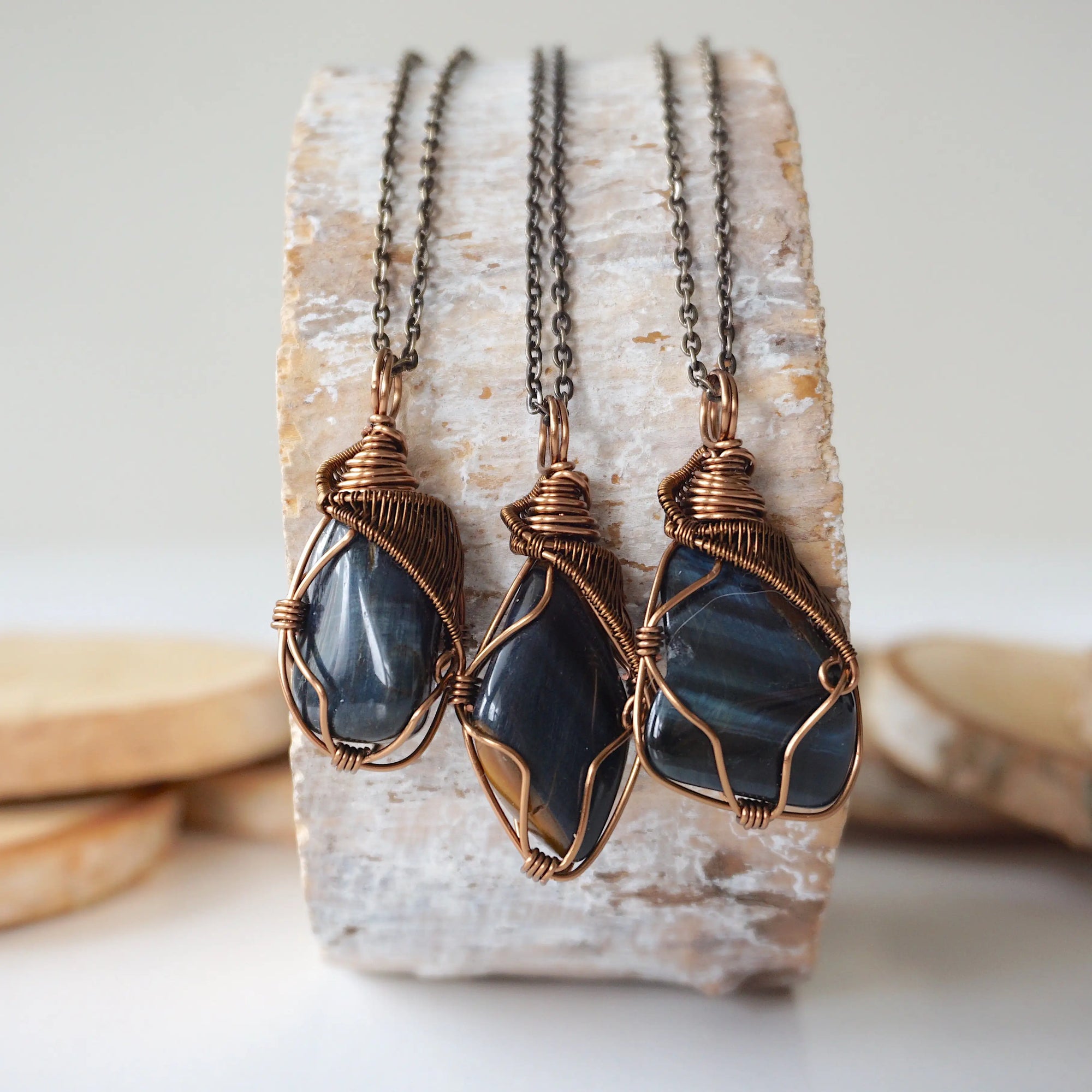 Three blue tiger's eye necklaces for men – showing natural variation in size, shape, and shade of blue, antique bronze copper wire wrapping.