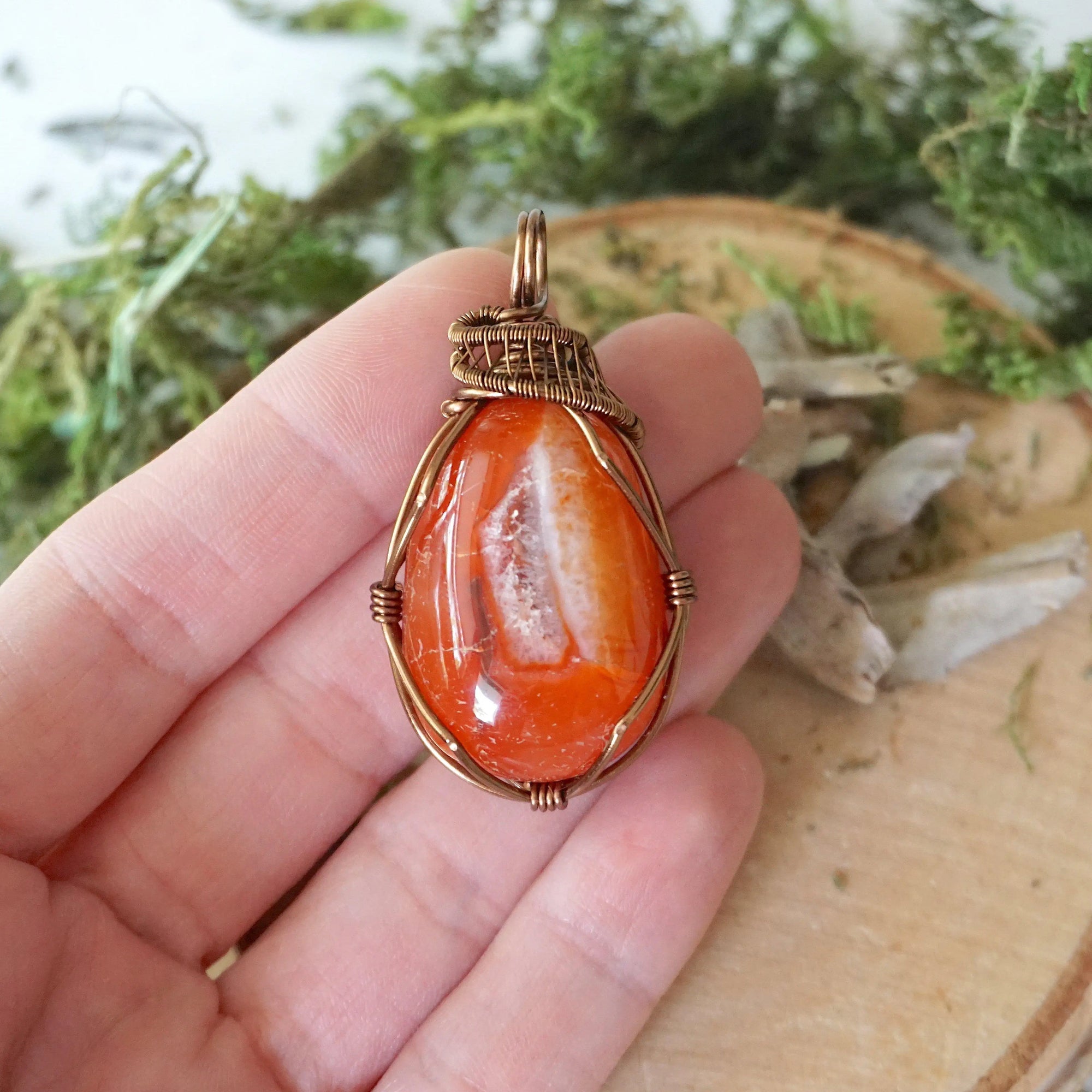 Carnelian pendant in hand for size reference – natural orange crystal, bronze copper wire, unisex Virgo birthstone jewelry by Designs by Nature Gems.