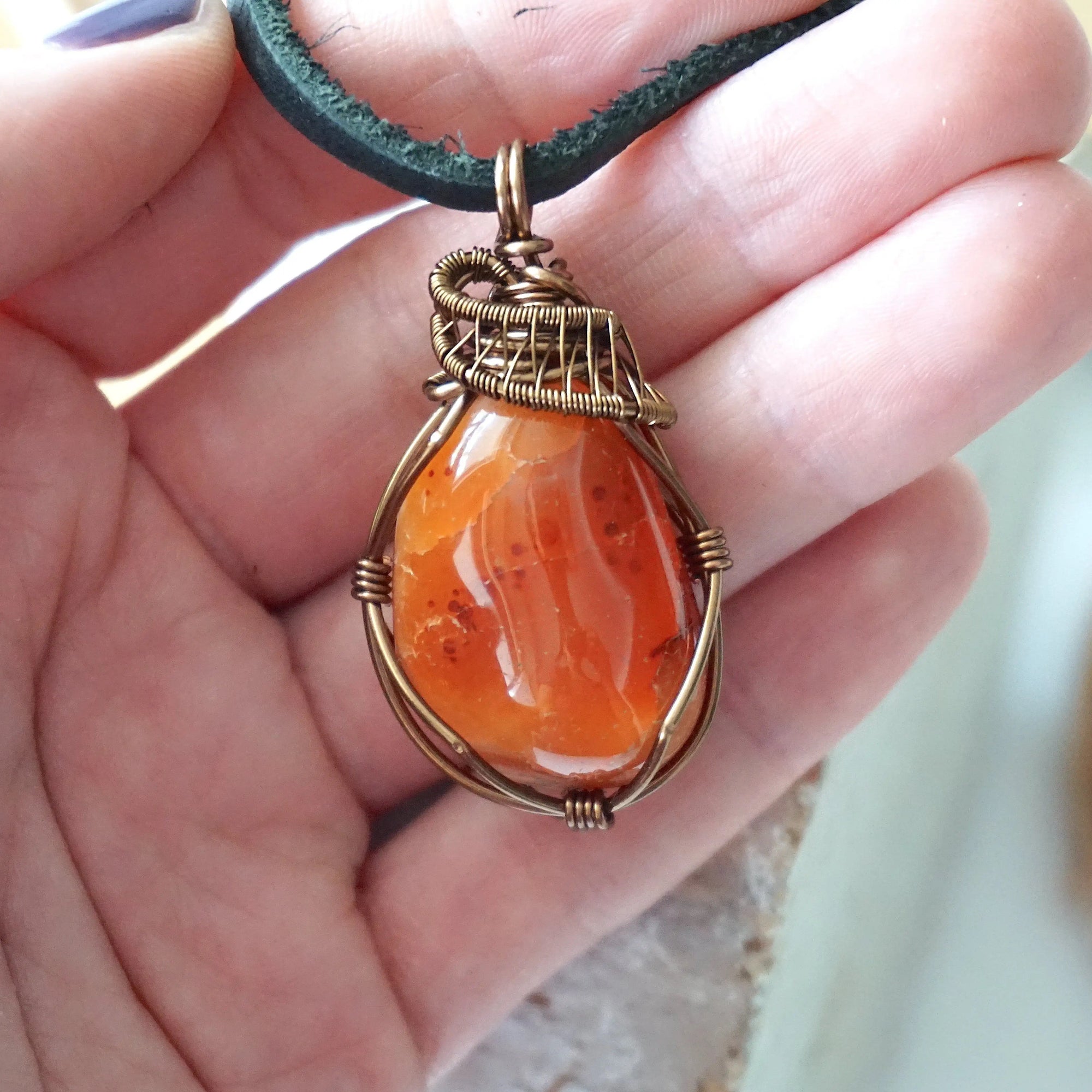 Carnelian pendant for men in hand for size reference – natural orange crystal, bronze copper wire, black leather cord, Virgo birthstone.