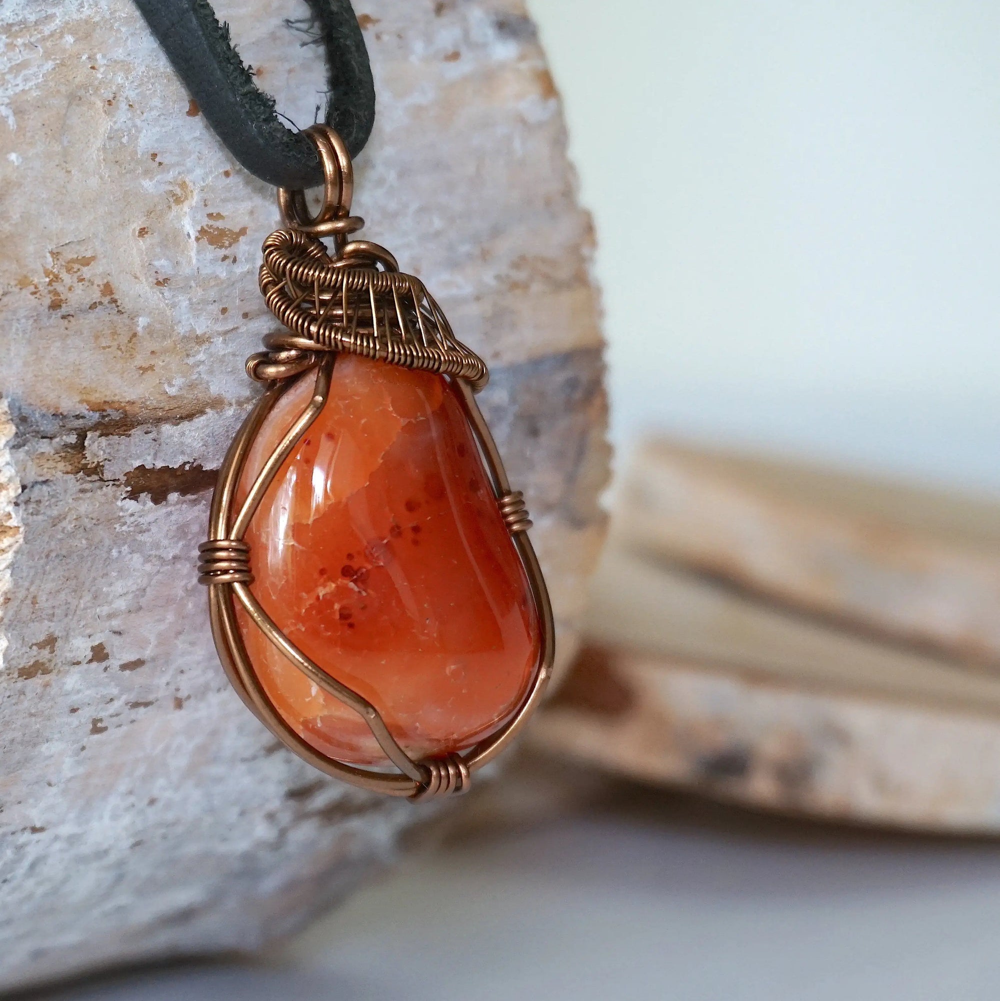 Right angle close-up of men's carnelian necklace – detailed bronze copper wire wrapping, raw carnelian, black leather cord.