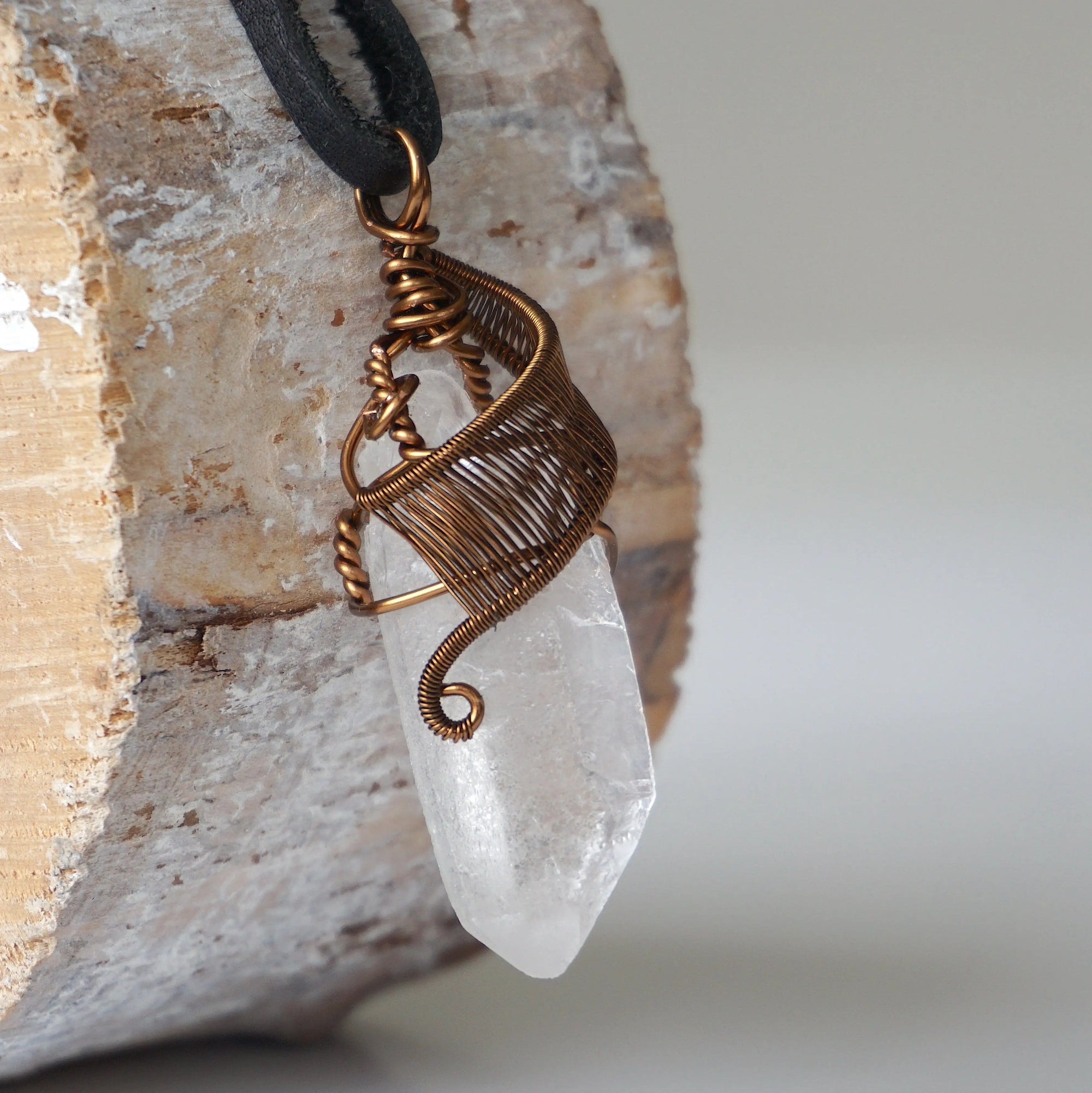 Right angle close-up of clear quartz point necklace for men – detailed antique bronze copper wire wrapping, natural quartz crystal, black leather cord.