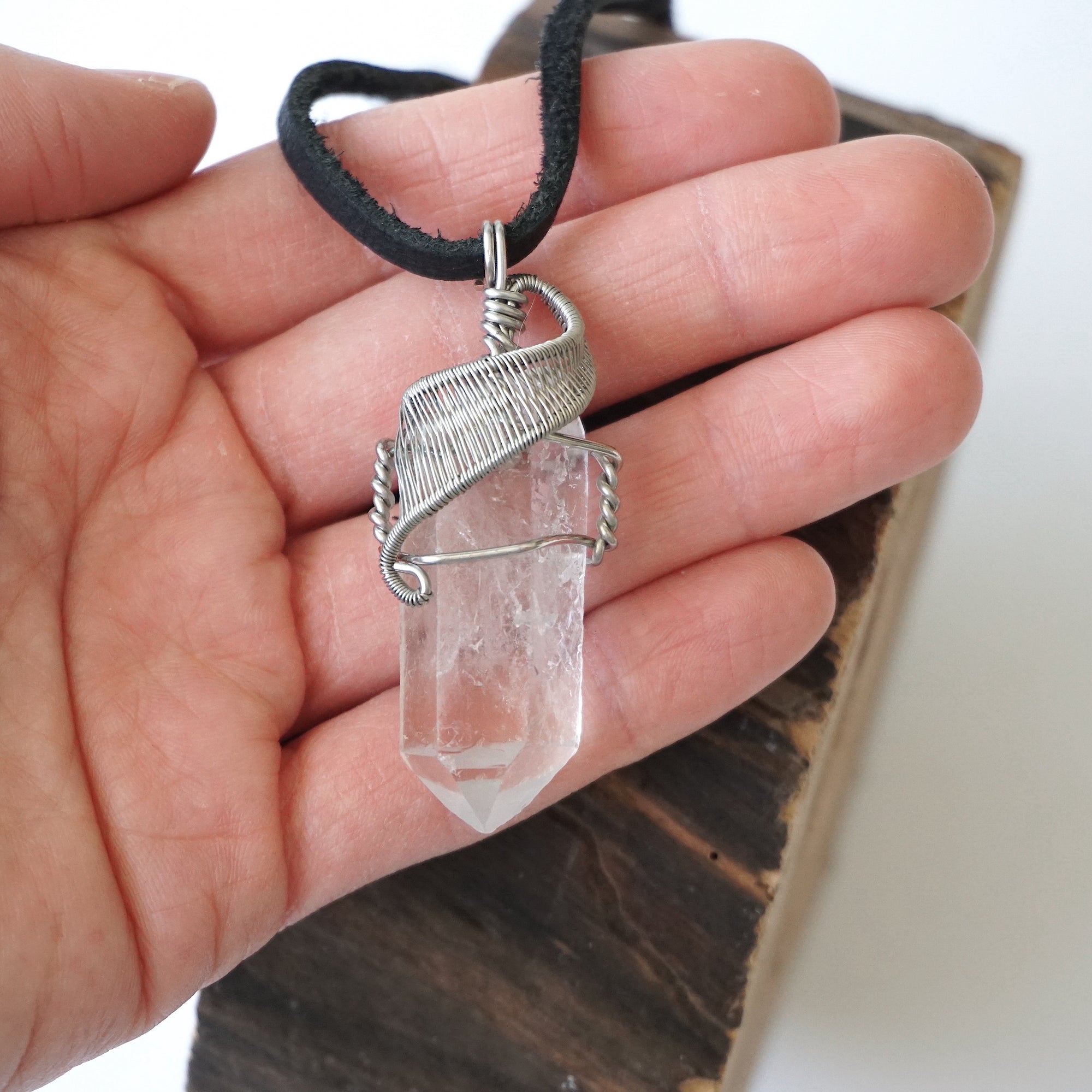 Clear quartz point pendant in hand for size reference – natural crystal, white gold copper wire, April birthstone, masculine design.