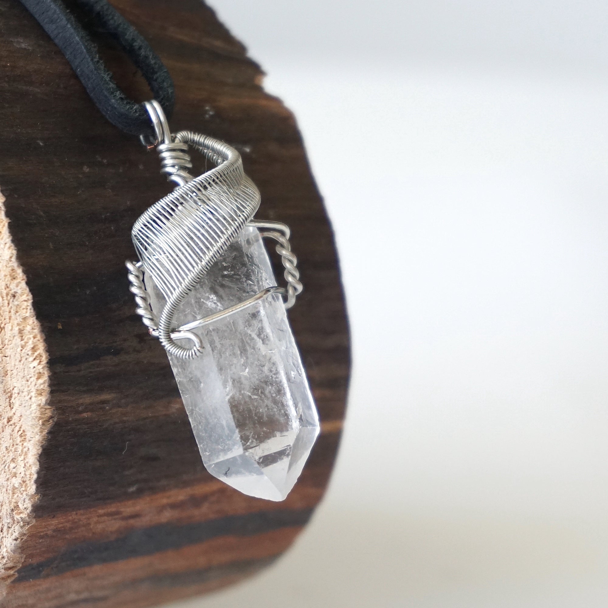 Right angle close-up of clear quartz point necklace for men – detailed white gold copper wire wrapping, natural quartz crystal, black leather cord.