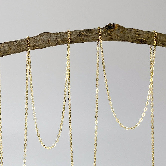 Gold chains hanging from a branch on a light gray background