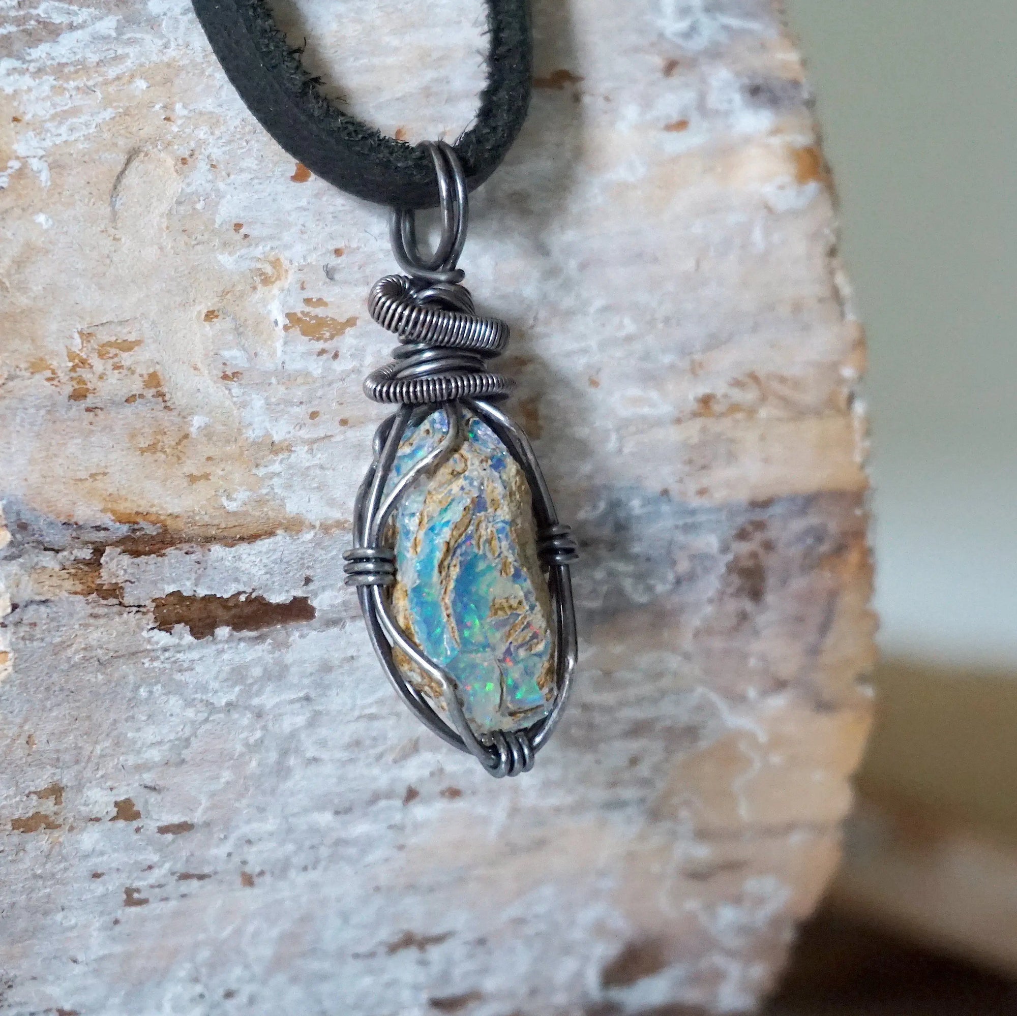 Right angle close-up of men's opal necklace – detailed antiqued sterling silver wire wrapping, raw opal, black leather cord.