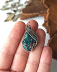 Peacock ore pendant in hand for size reference – natural raw bornite, white gold copper wire wrapping, Capricorn and Cancer birthstone, feminine design.