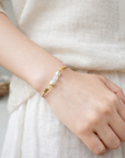 Hand wearing a pearl bracelet on a neutral background