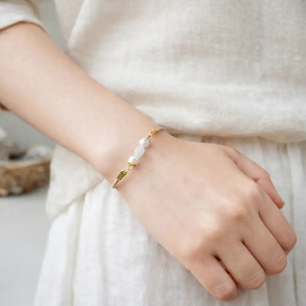 Hand wearing a pearl bracelet on a neutral background