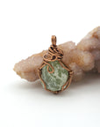 Copper pendant with green stone on a rock formation