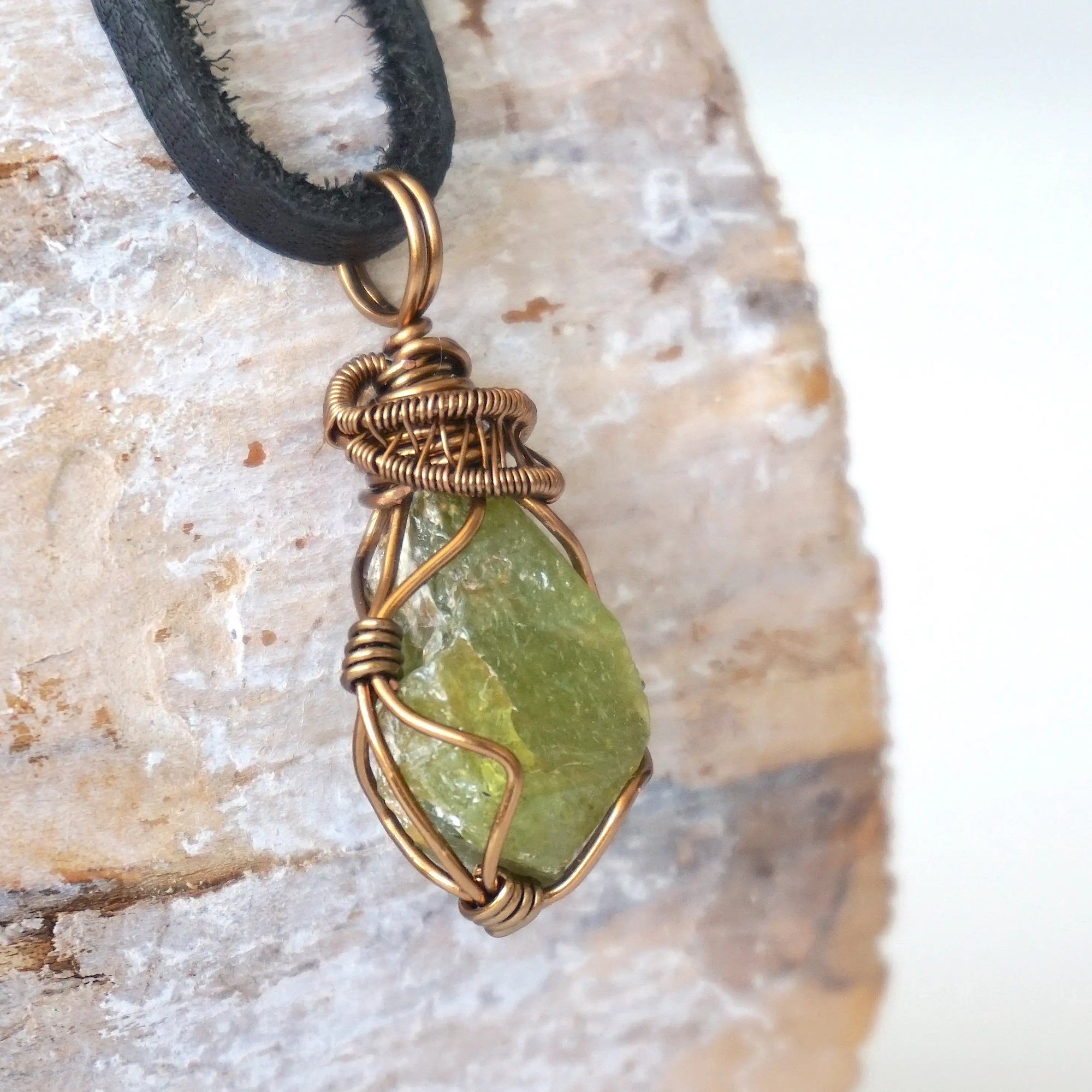 Right angle close-up of men's peridot necklace – detailed bronze copper wire wrapping, raw peridot, black leather cord.