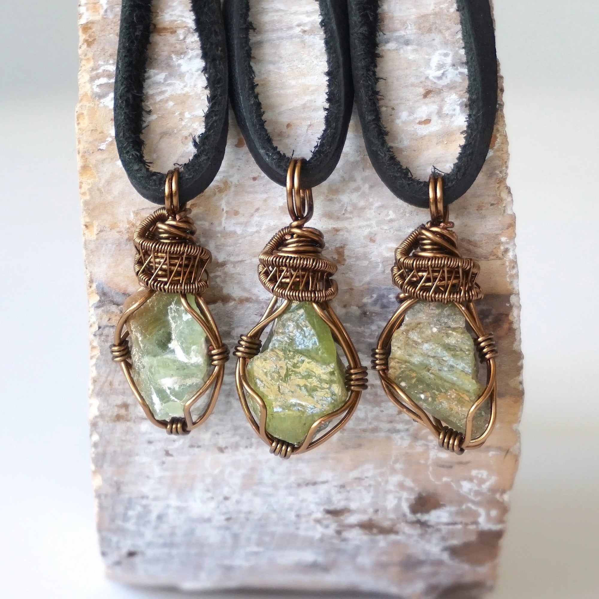 Three raw peridot pendants for men – showing natural variation in size, shape, and green shade, black leather cord.