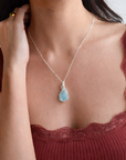 Necklace with a blue gemstone pendant worn by a person in a red top.