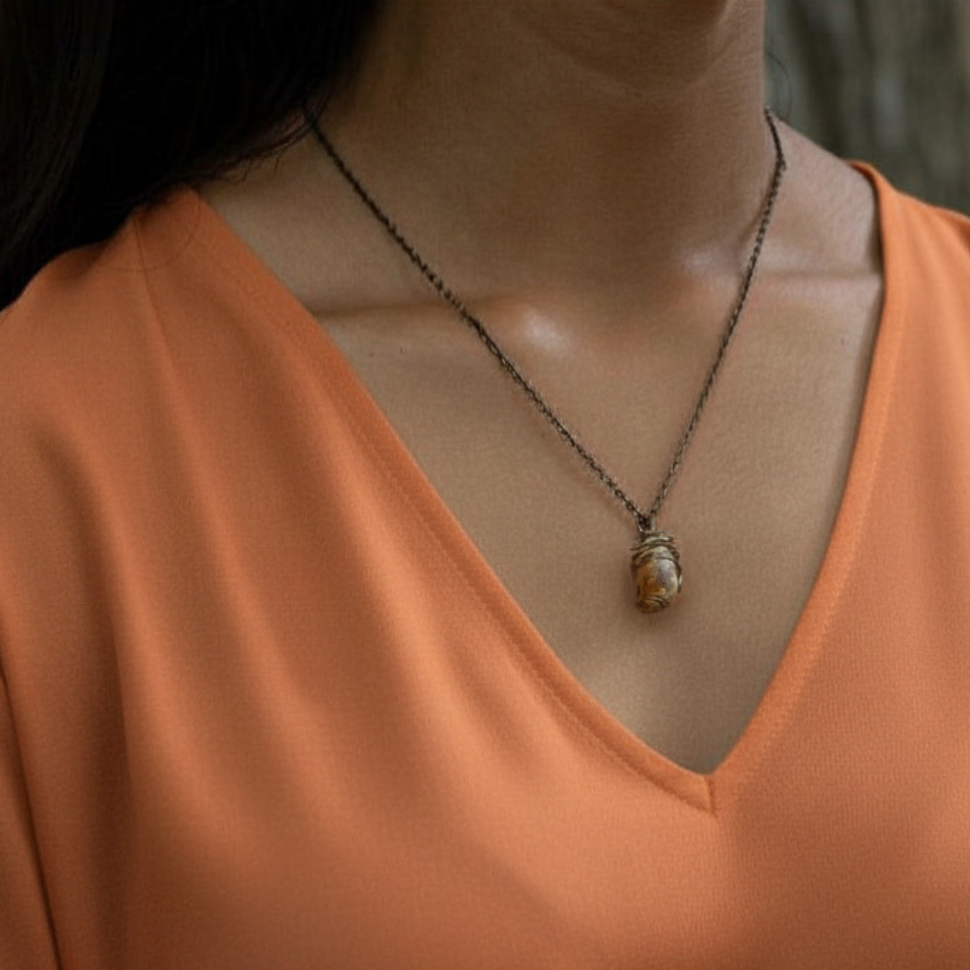 Necklace with a pendant worn by a person in an orange top.