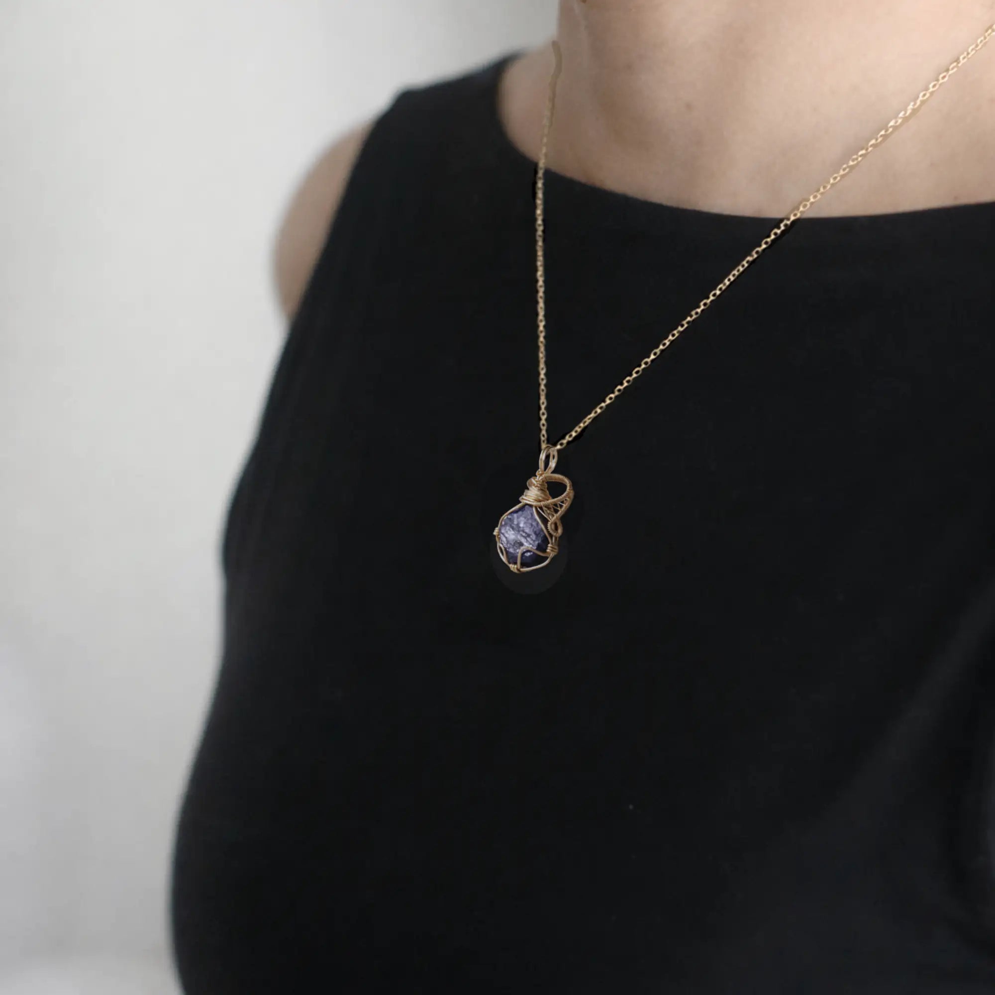 Sapphire gold necklace with a pendant on a black top against a white background