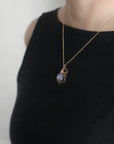 Sapphire gold necklace with a pendant on a black top against a white background