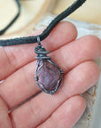 Ruby pendant for men in hand for size reference – natural red crystal, antiqued sterling silver wire, black leather cord, July birthstone.