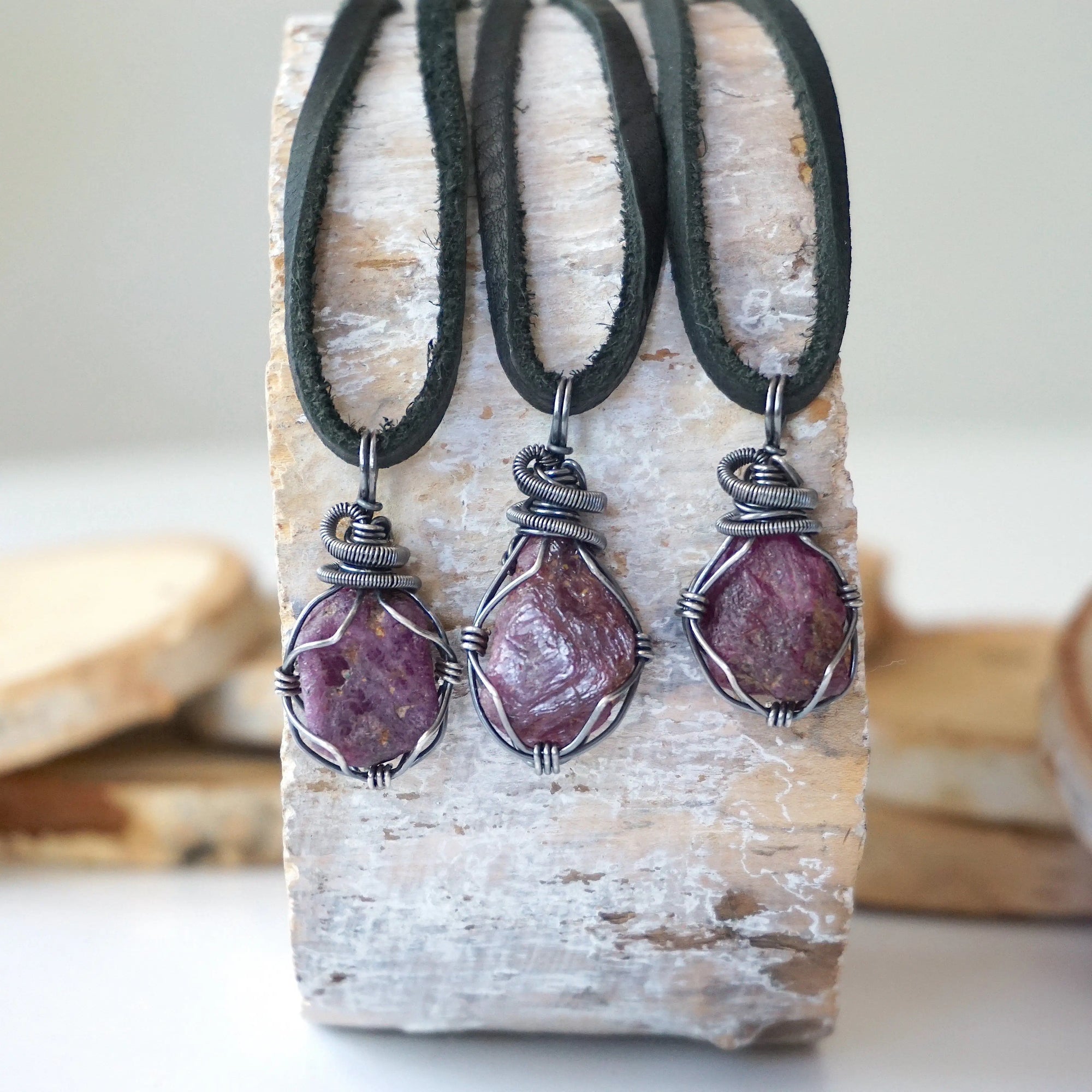 Three raw ruby pendants for men – showing natural variation in size, shape, and red shade, black leather cord.