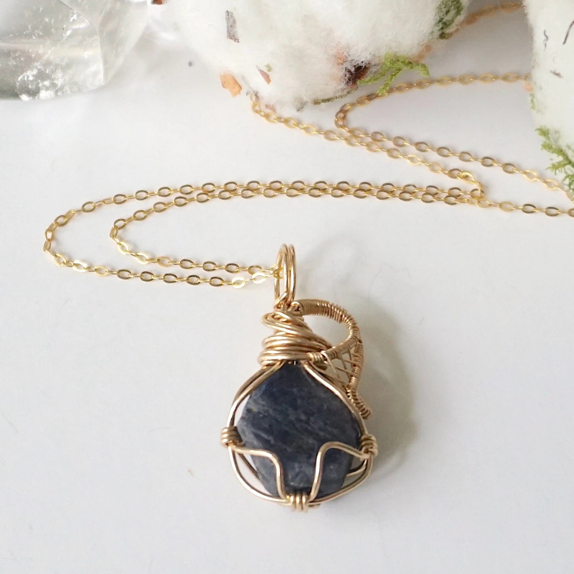 Necklace with a gold-wrapped dark blue sapphire stone pendant on a light background