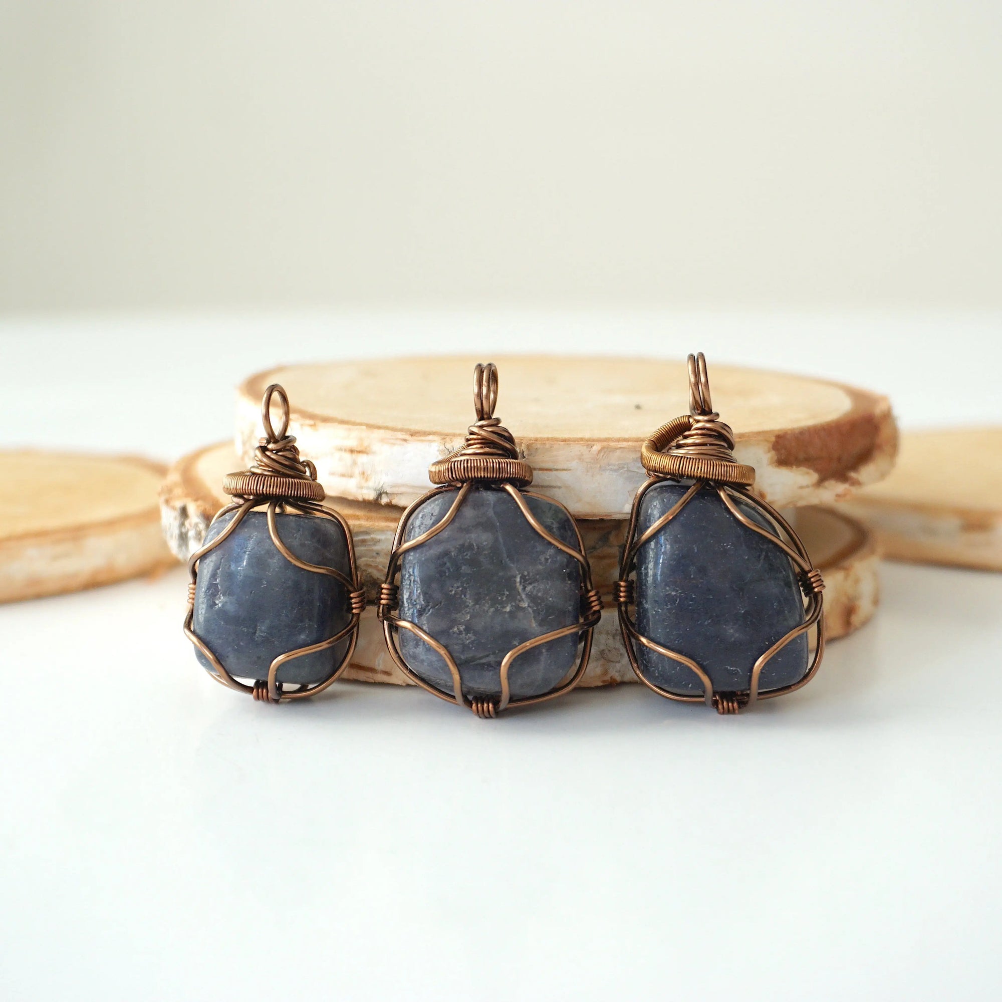 Three raw sapphire pendants – showing natural variation in size, shape, and blue shade, handcrafted unisex birthstone jewelry.