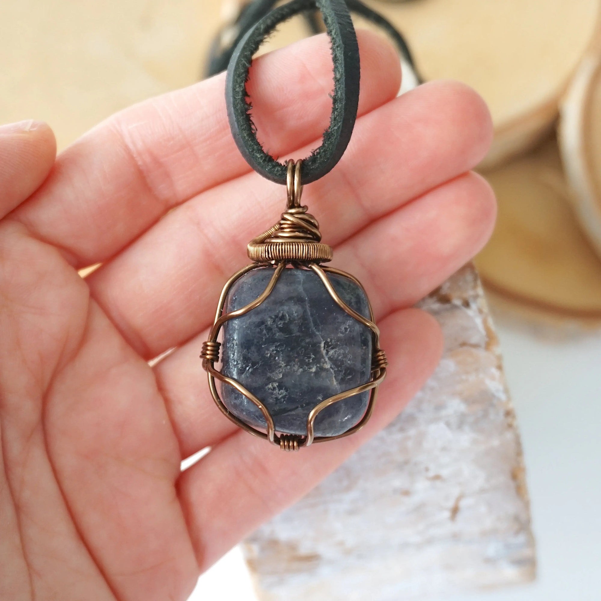 Sapphire pendant for men in hand for size reference – genuine raw sapphire, bronze copper wire, black leather cord, September birthstone.