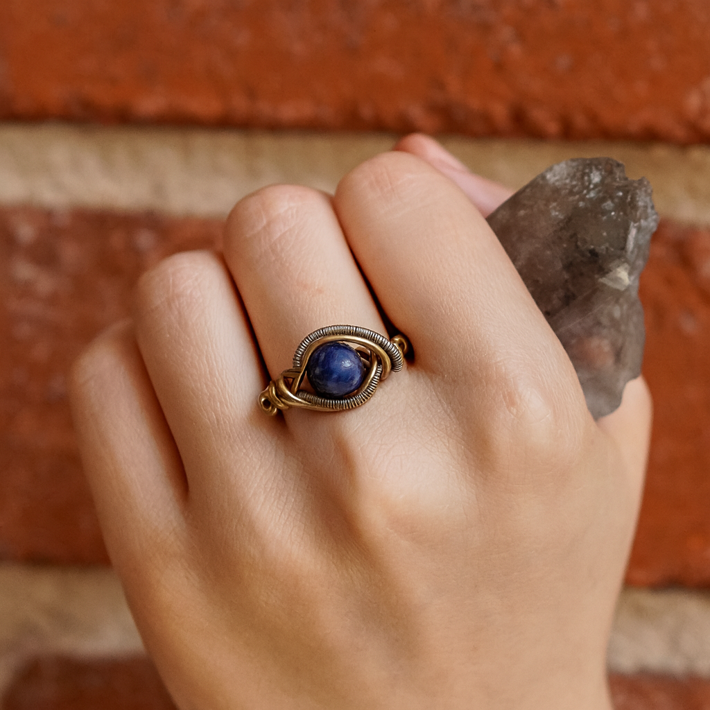 Hand wearing a gold ring with a blue stone against a brick wall background