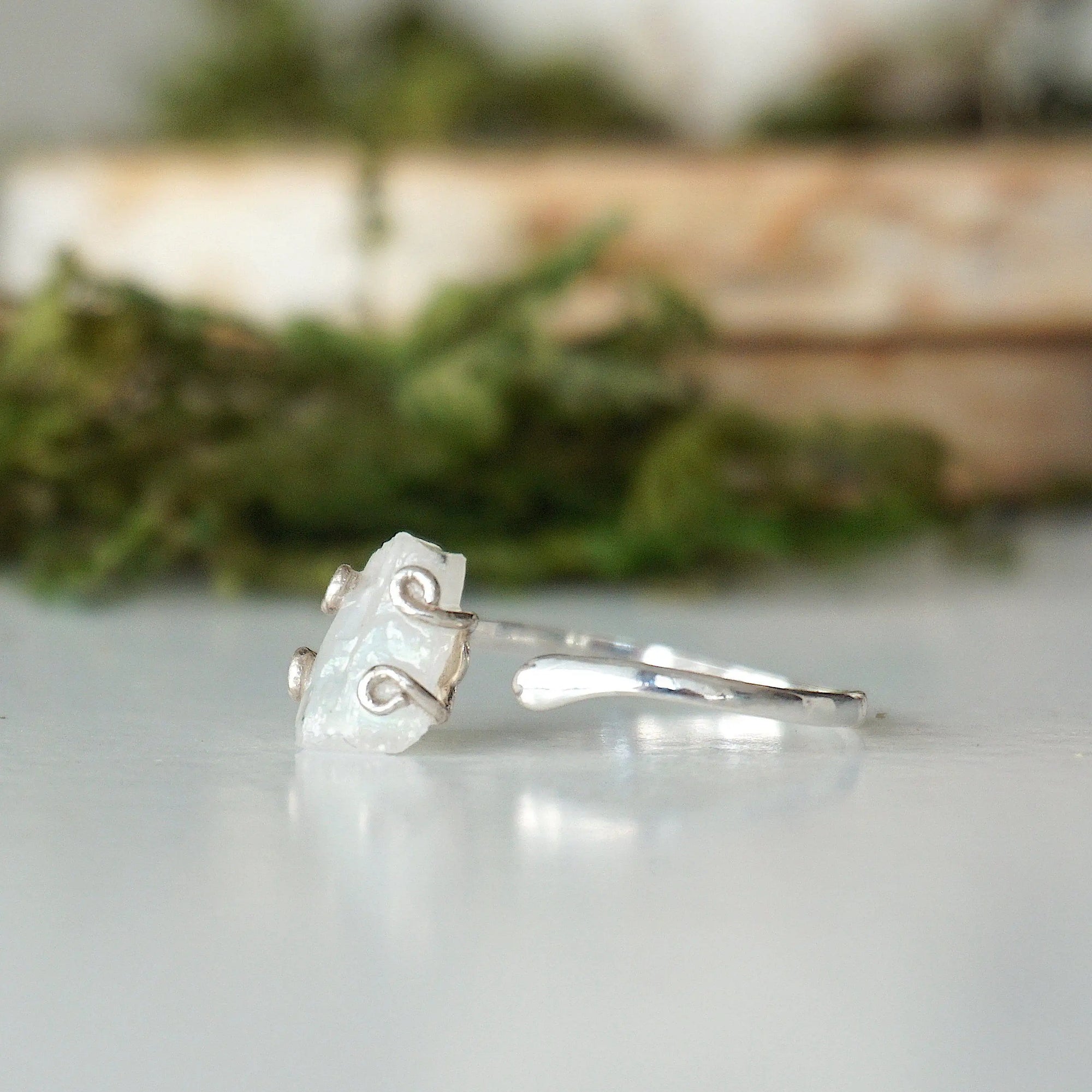 Left side angle close-up of adjustable raw rainbow moonstone ring highlighting organic moonstone profile and sterling silver setting.