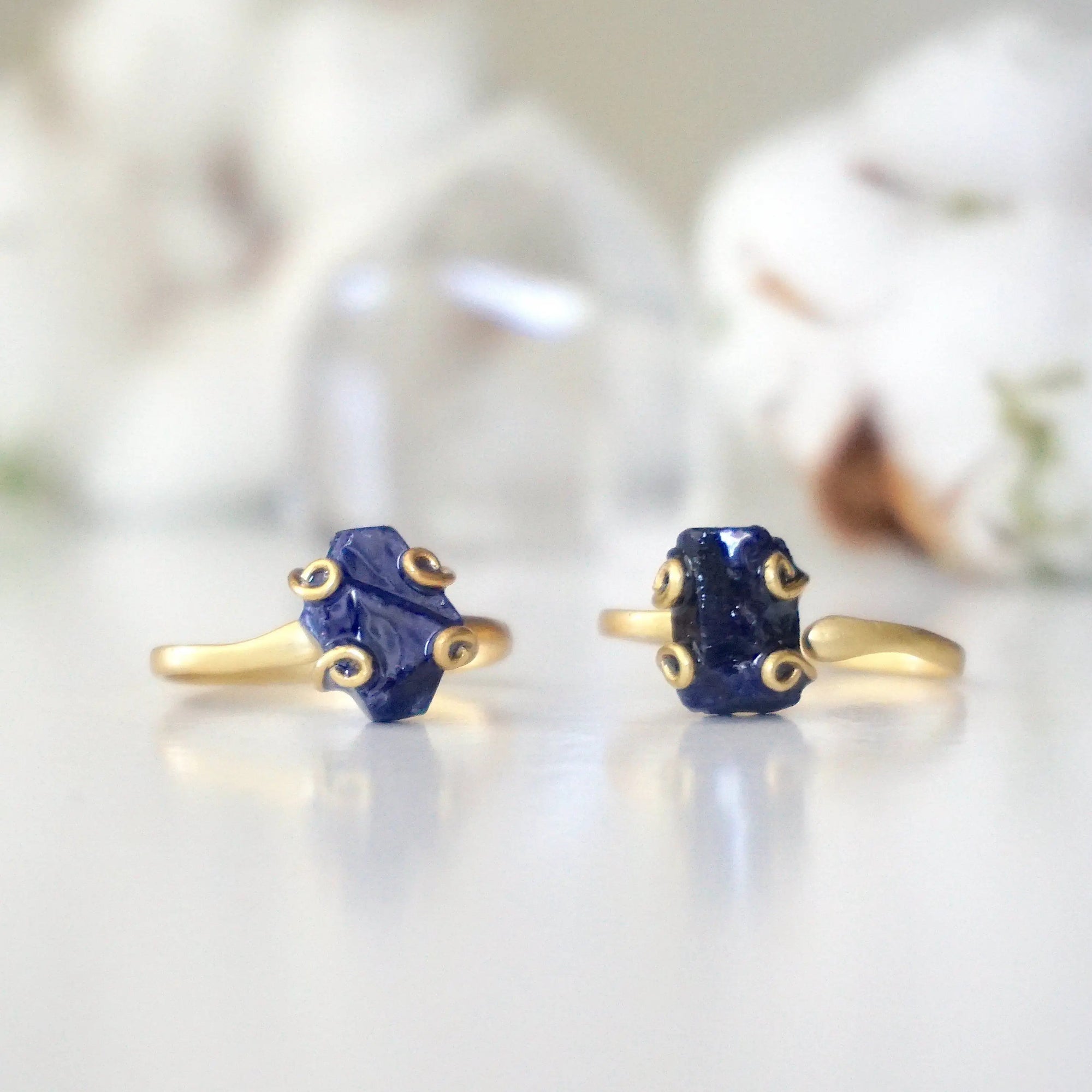 Two adjustable raw sapphire rings showing natural variation in stone size, shape, markings, and blue colour — each ring is one of a kind