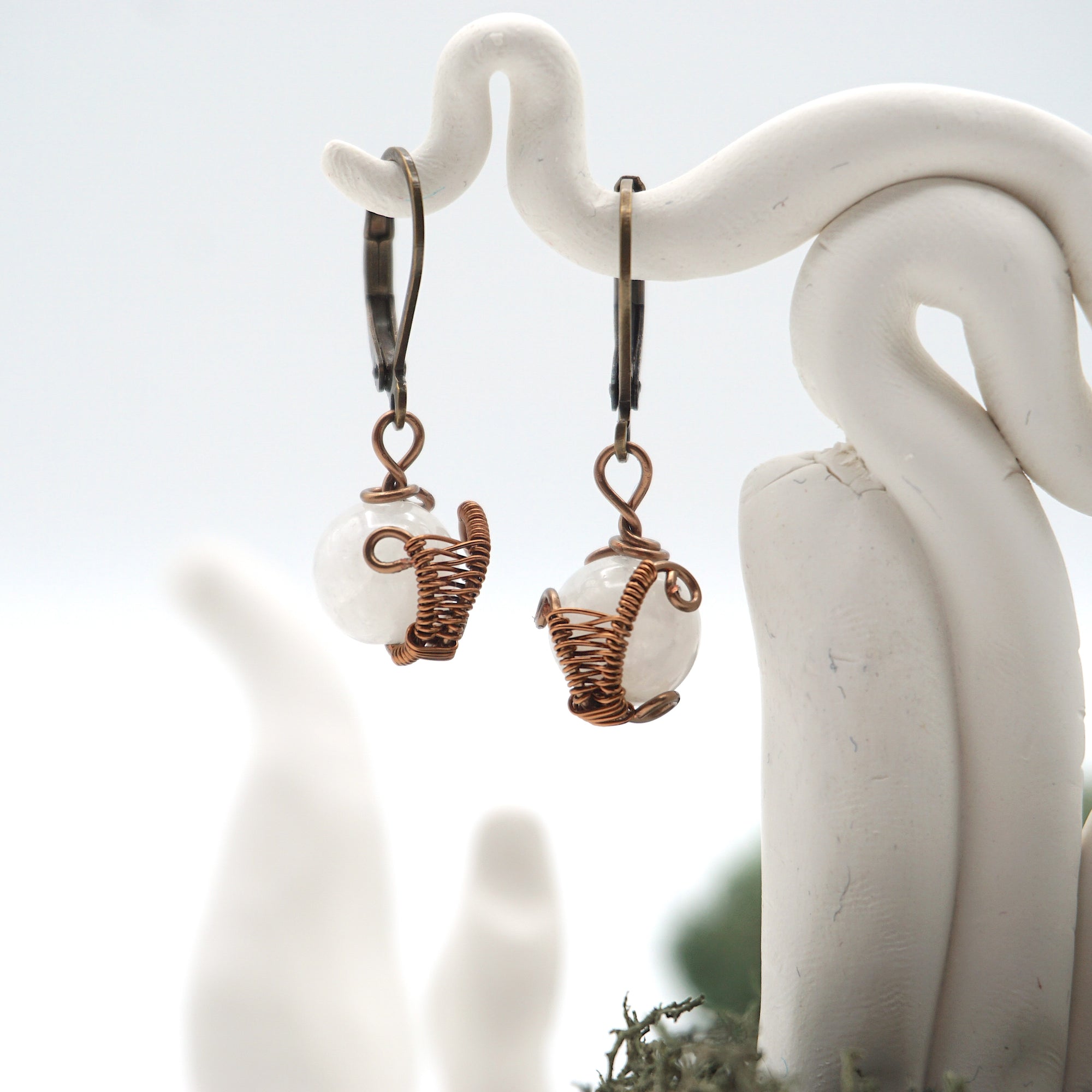 Front angle of rainbow moonstone drop earrings hanging on a jewelry display, wire-wrapped design.