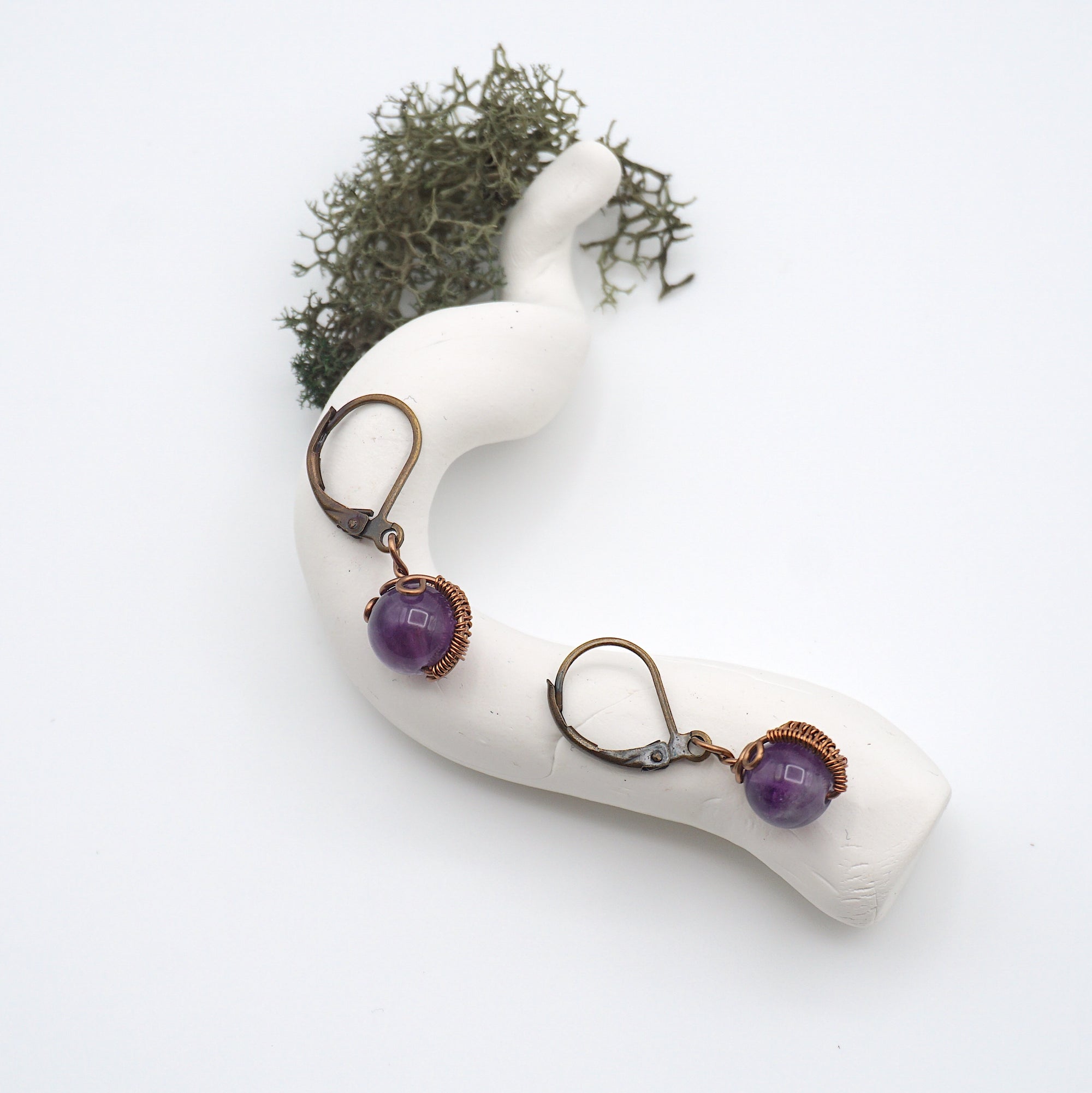 Bird’s eye view of amethyst drop earrings laying flat on a display, showing detailed wire wrapping and gemstone color.