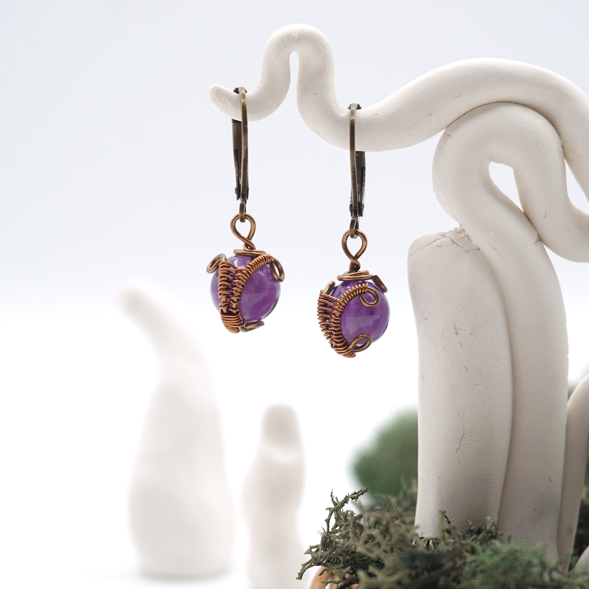 Close-up of handcrafted amethyst drop earrings with antique bronze copper wire wrapping.
