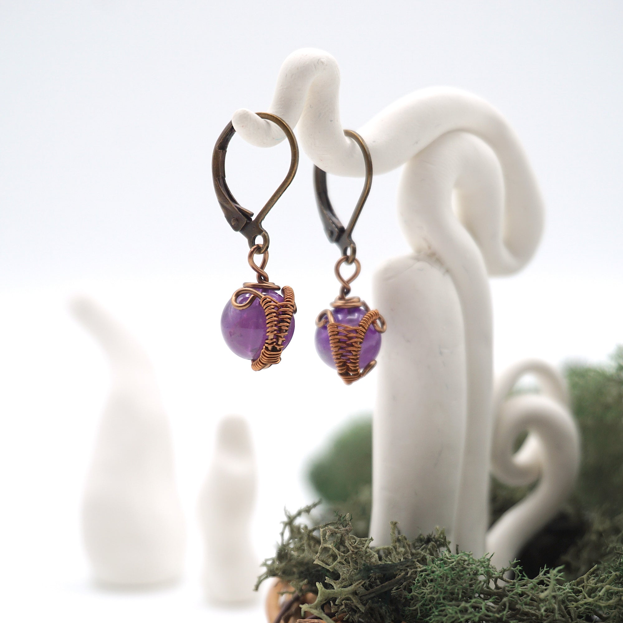 Side angle of amethyst drop earrings on a display stand, highlighting antique bronze copper wire wrapping.