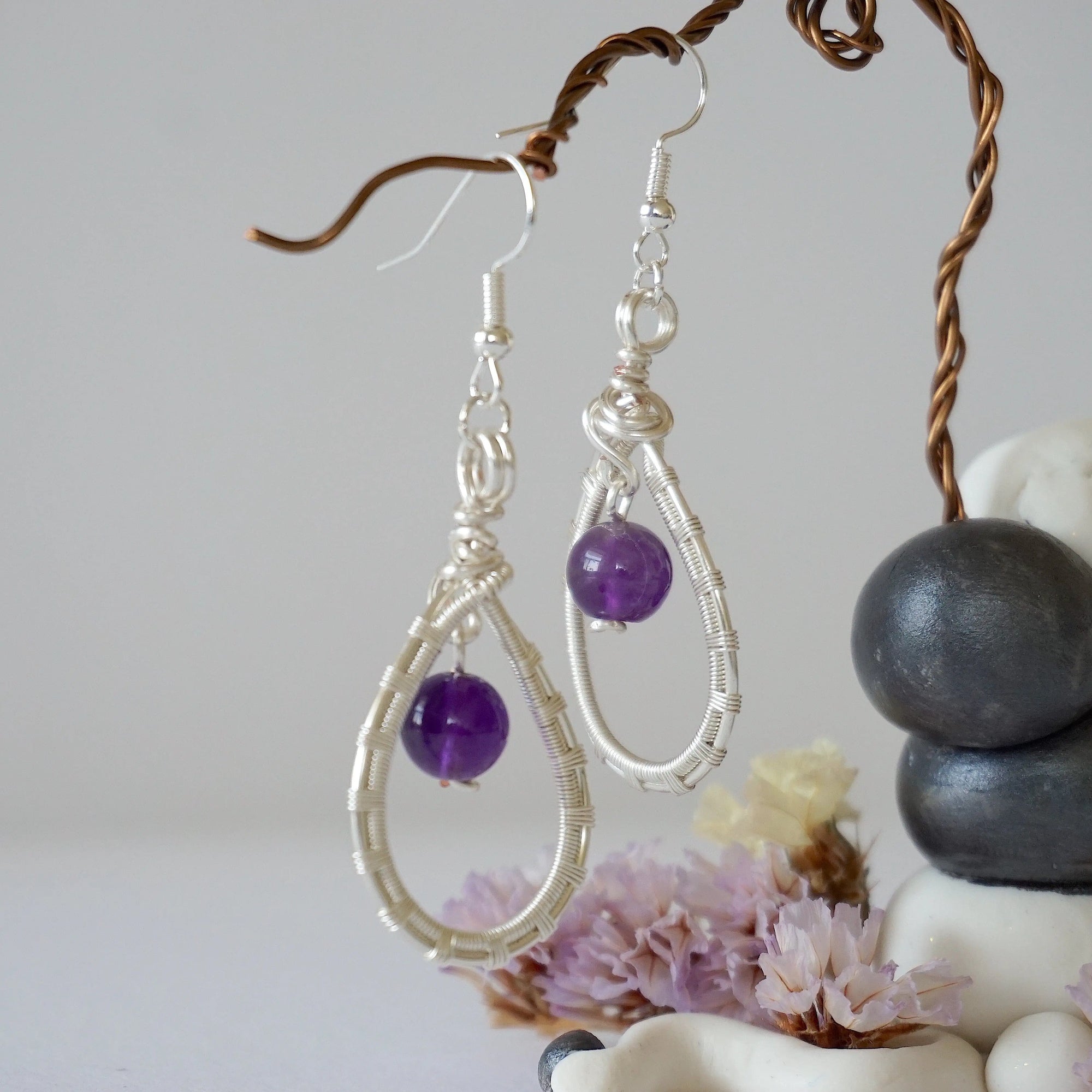 Side view of wire wrapped amethyst dangle earrings in silver plated copper with fish hook ear wires and teardrop frame