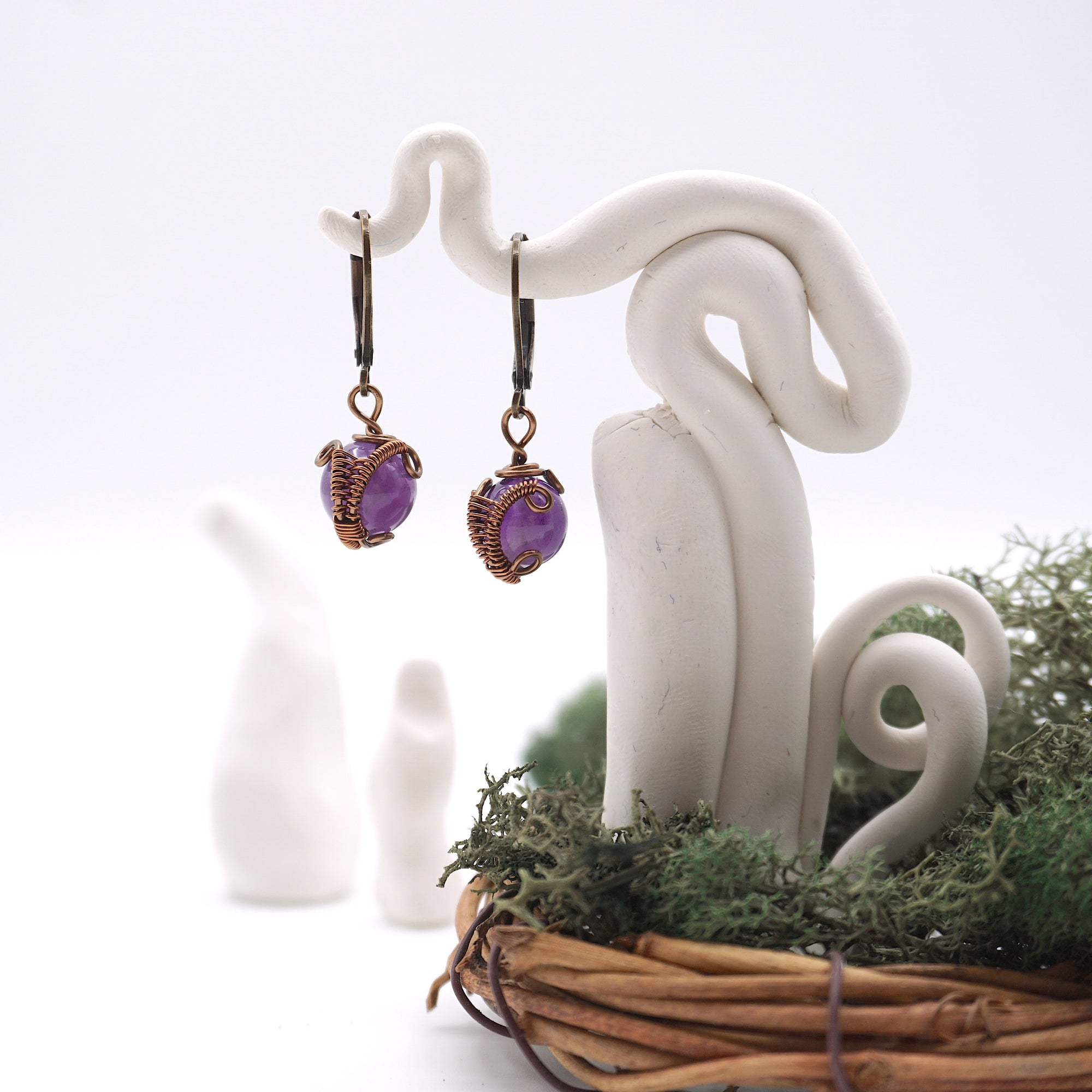 Front angle of amethyst drop earrings hanging on a jewelry display, wire-wrapped design.