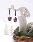 Front angle of amethyst drop earrings hanging on a jewelry display, wire-wrapped design.