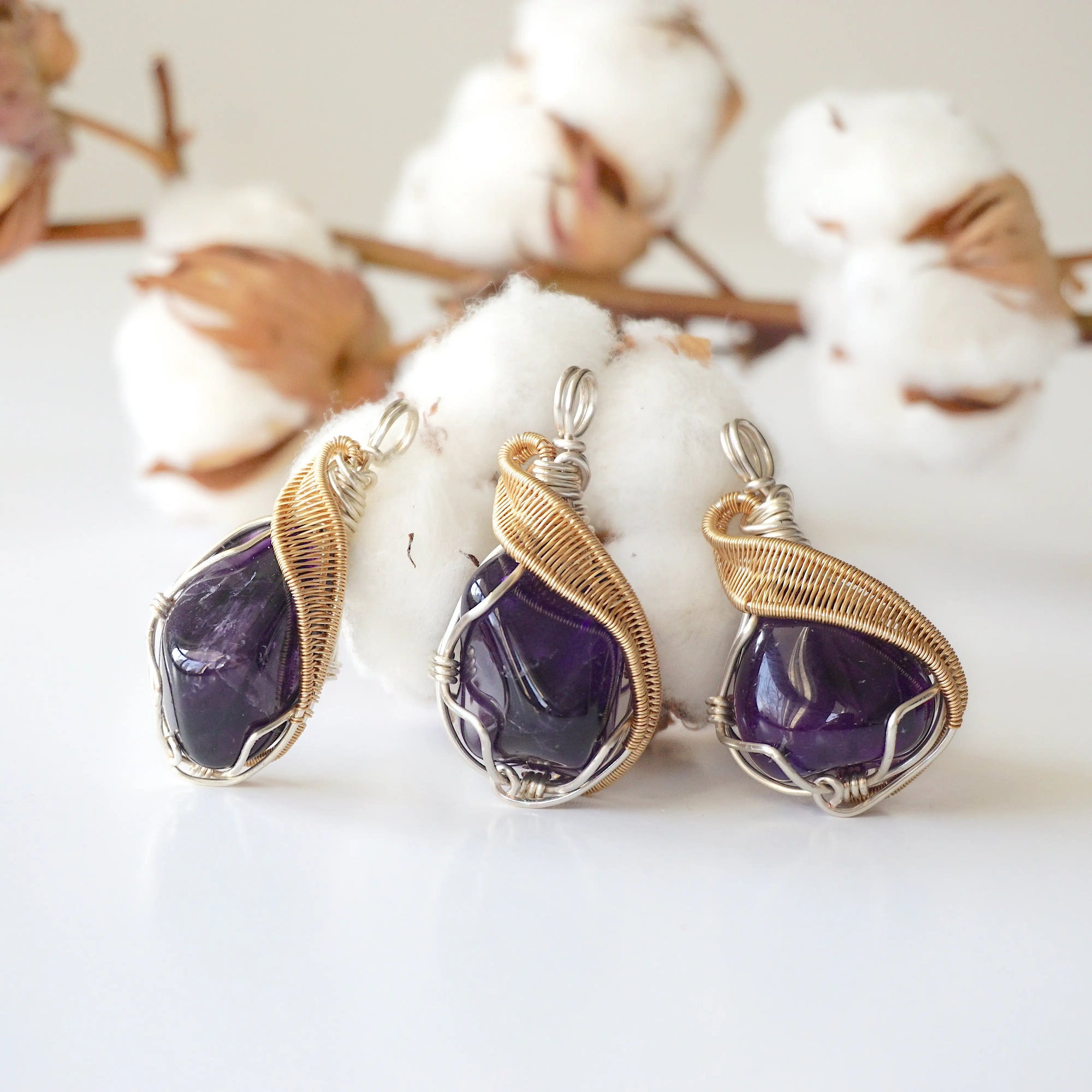 Three women’s amethyst pendants showing natural variation in stone size, shape, and color, silver and gold plated copper artisan wire wrap