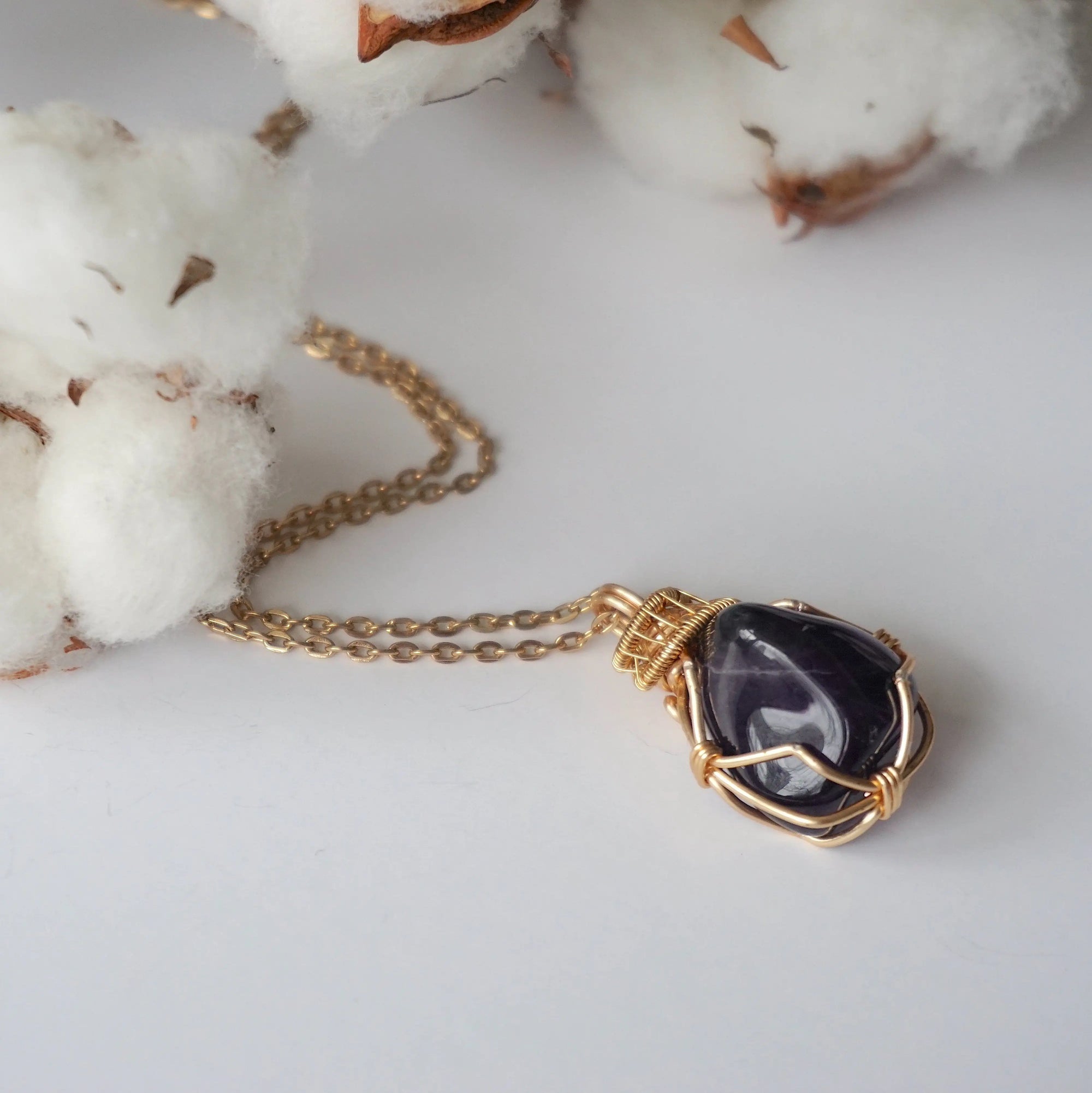 Detailed front view of women’s polished dark amethyst pendant on gold chain, artisan wire wrapped in gold plated copper