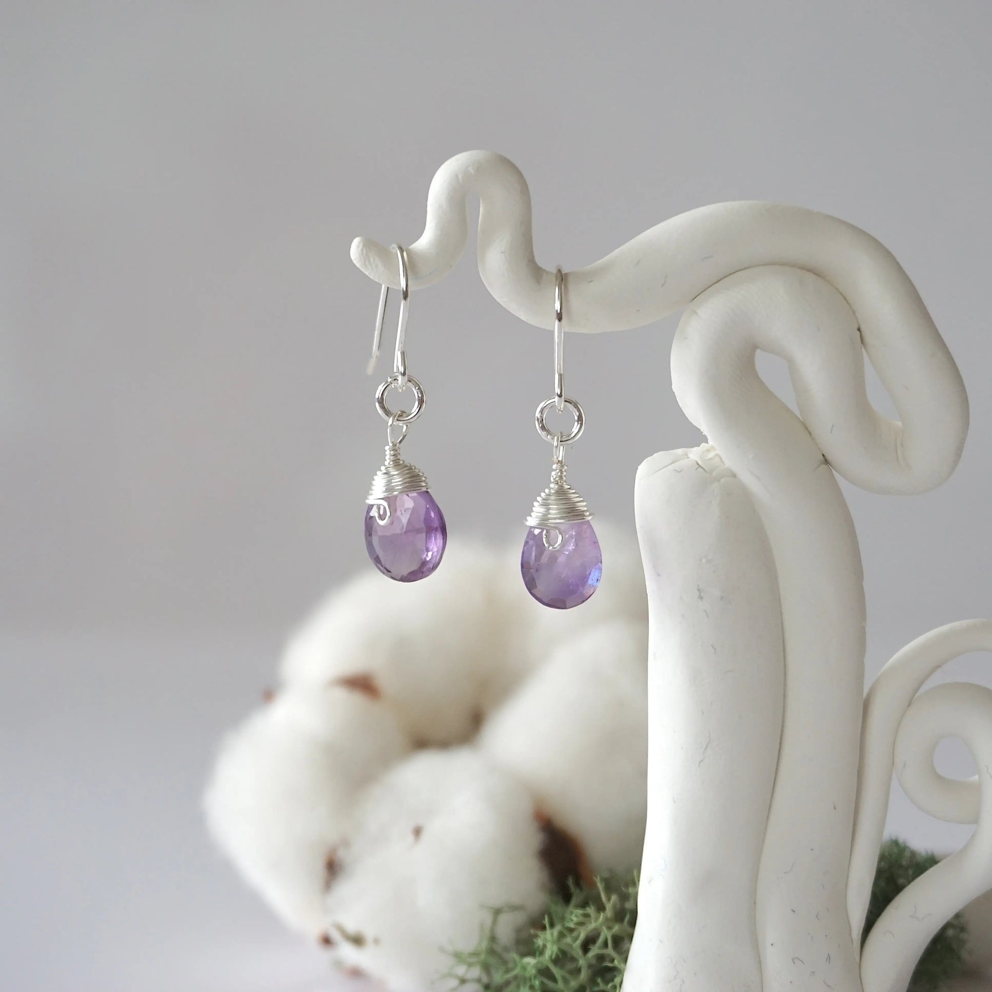 Detailed front view of handcrafted amethyst sterling silver drop earrings with natural faceted amethyst, artisan wire wrapping, hanging from a display – Designs by Nature Gems